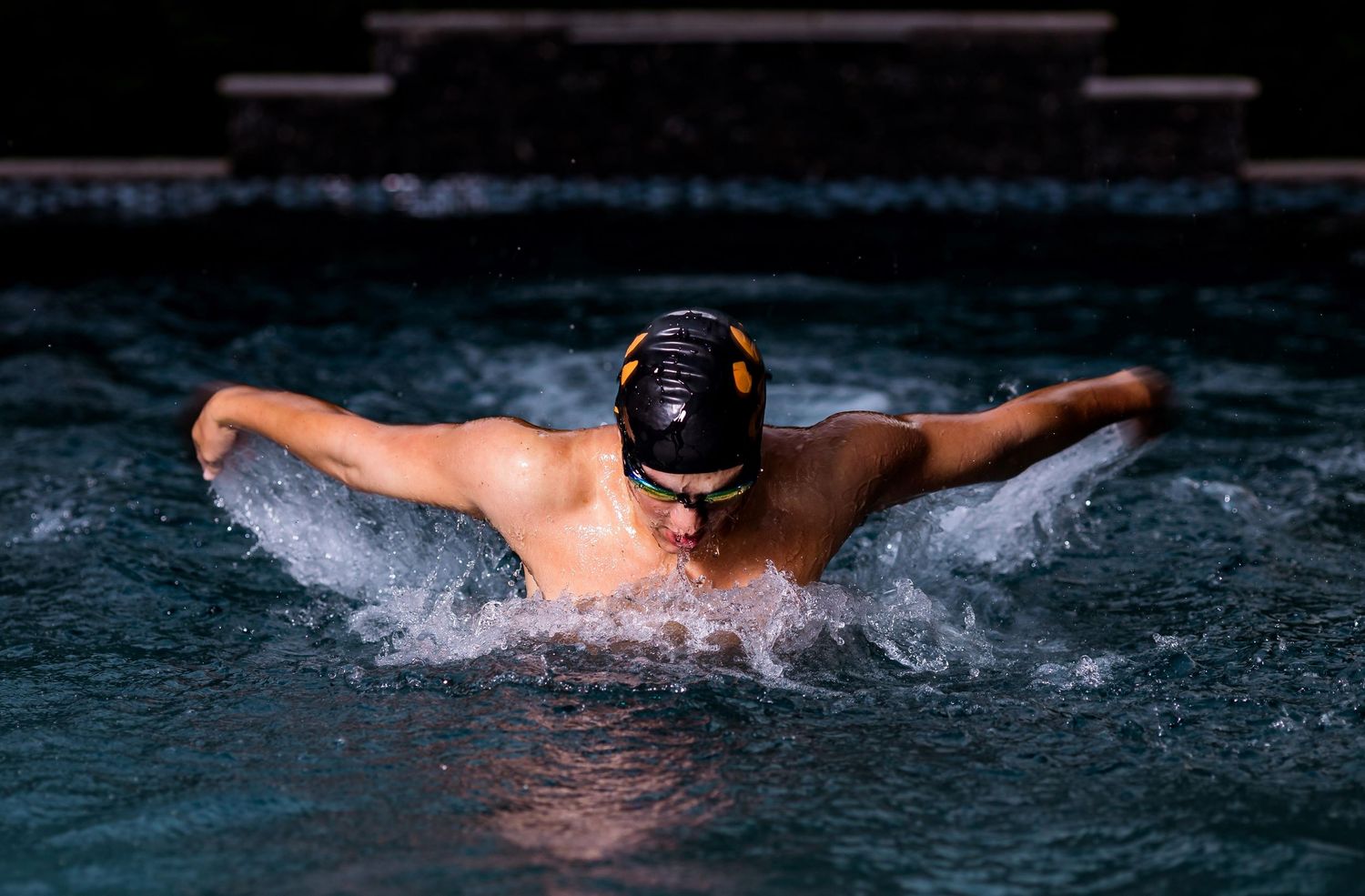 Multiple action shots of a swimmer performing butterfly stroke movements in dark blue pool water.