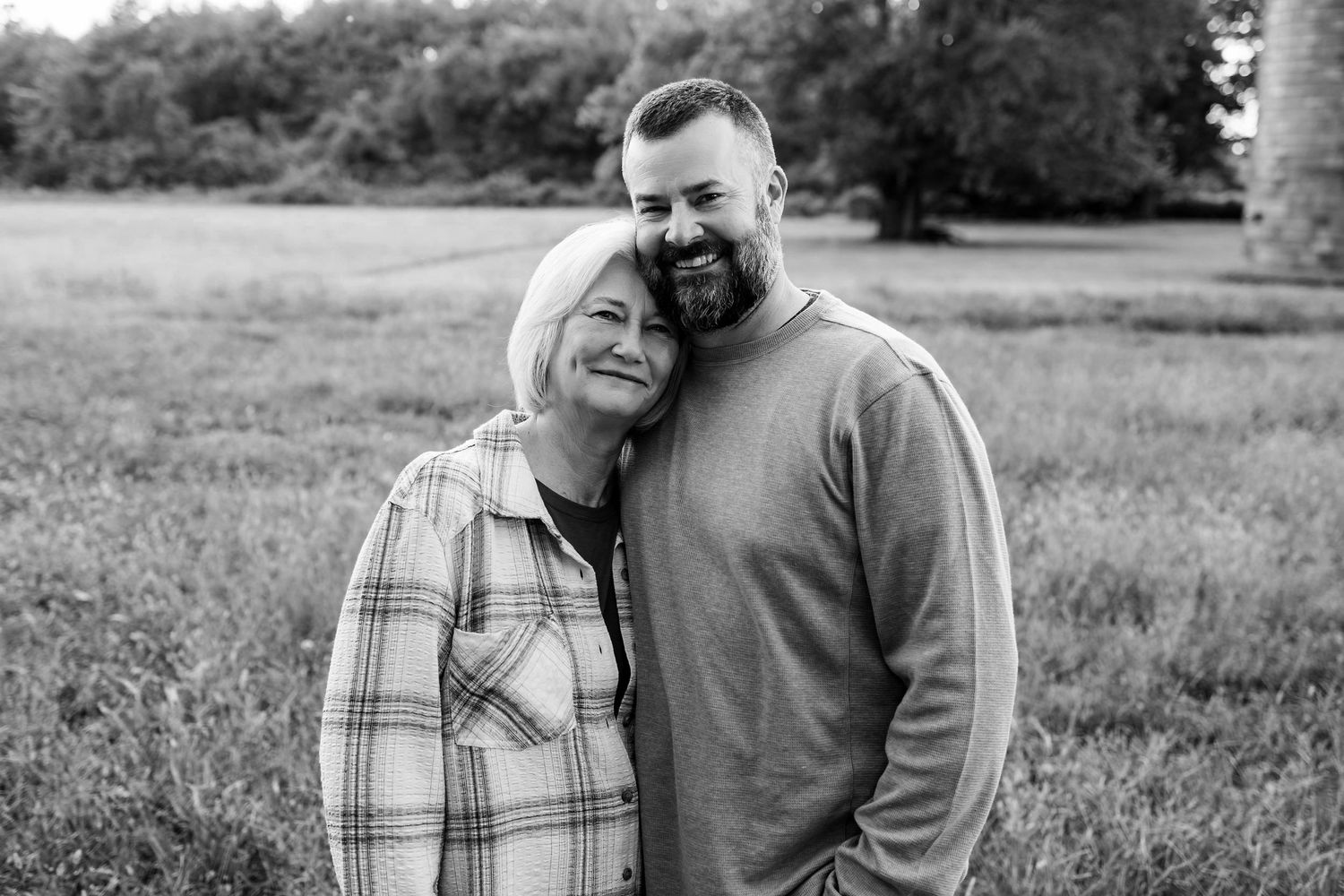 Black and white portrait of a couple embracing outdoors in a grassy field on a sunny day.