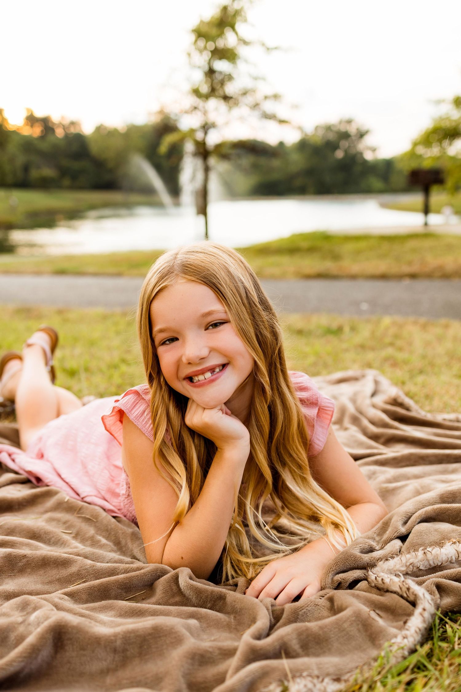 A series of outdoor portraits showing a child lying on a brown blanket in a grassy field during golden hour.