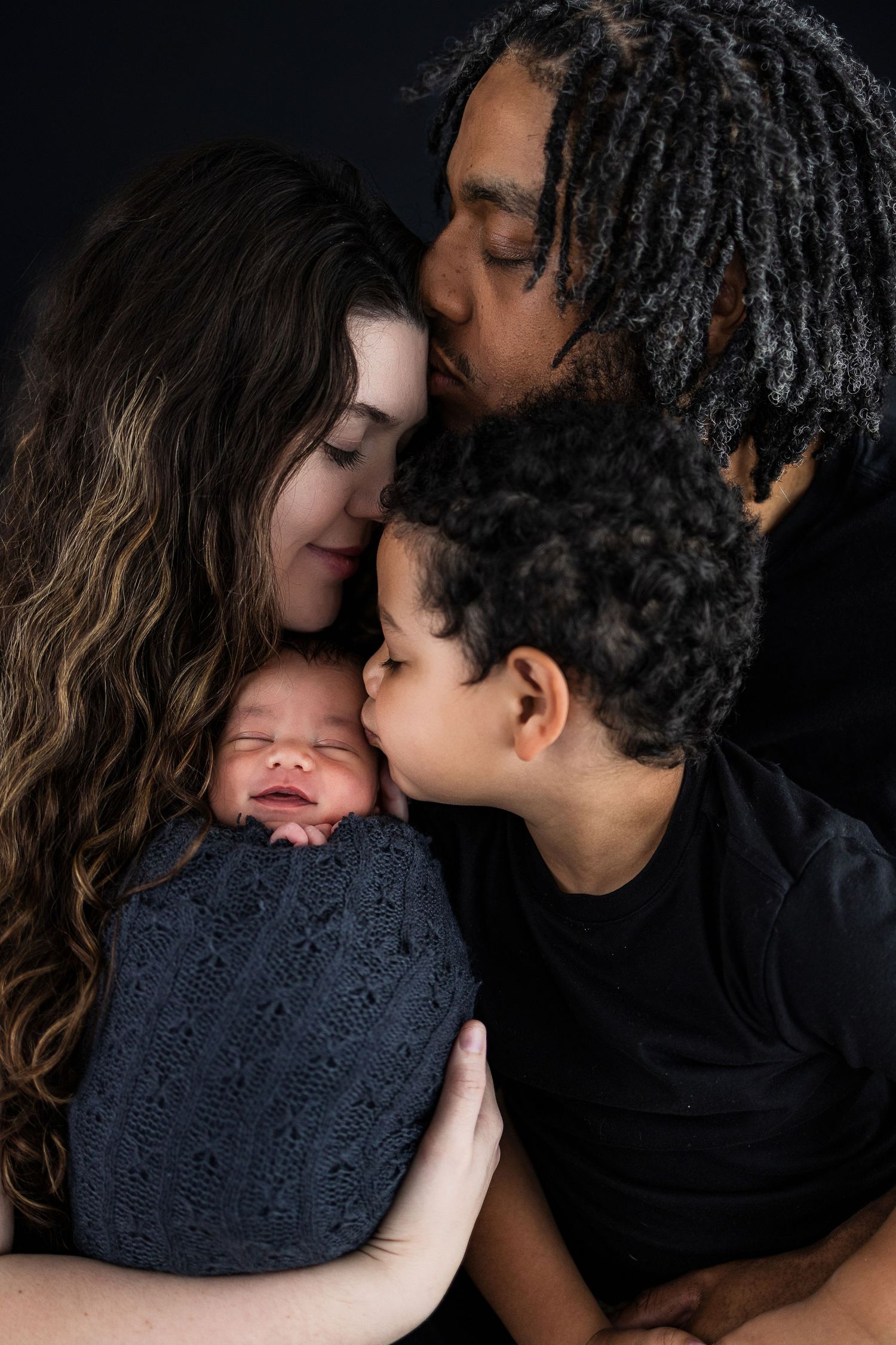 A tender moment as a family shares loving snuggles with their newborn baby wrapped in a navy blue knit blanket.
