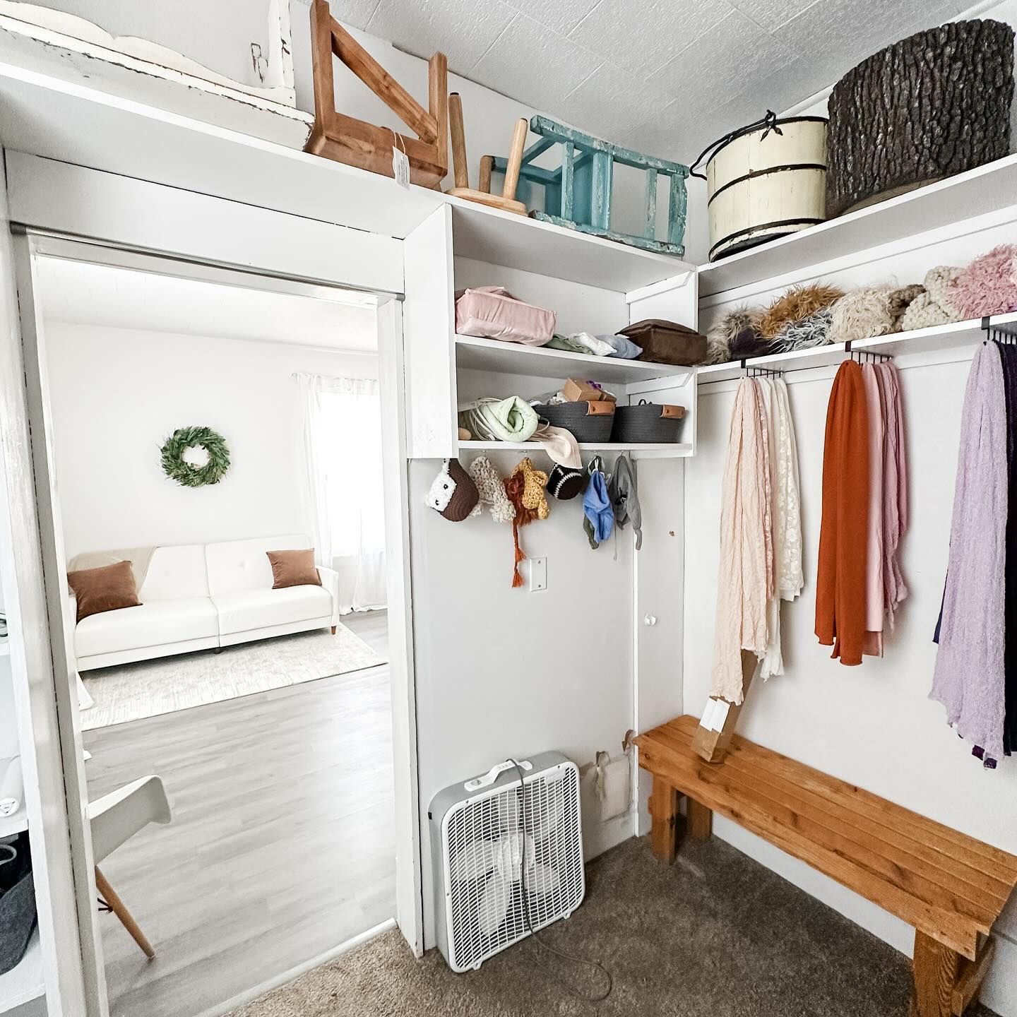 Modern closet space with white shelving, wooden bench and clothing storage.