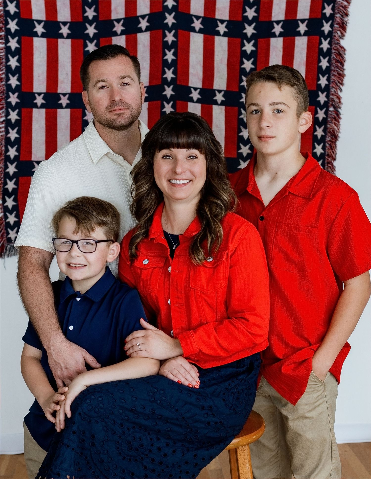 Family of four photographed against an American flag backdrop during a patriotic studio portrait session