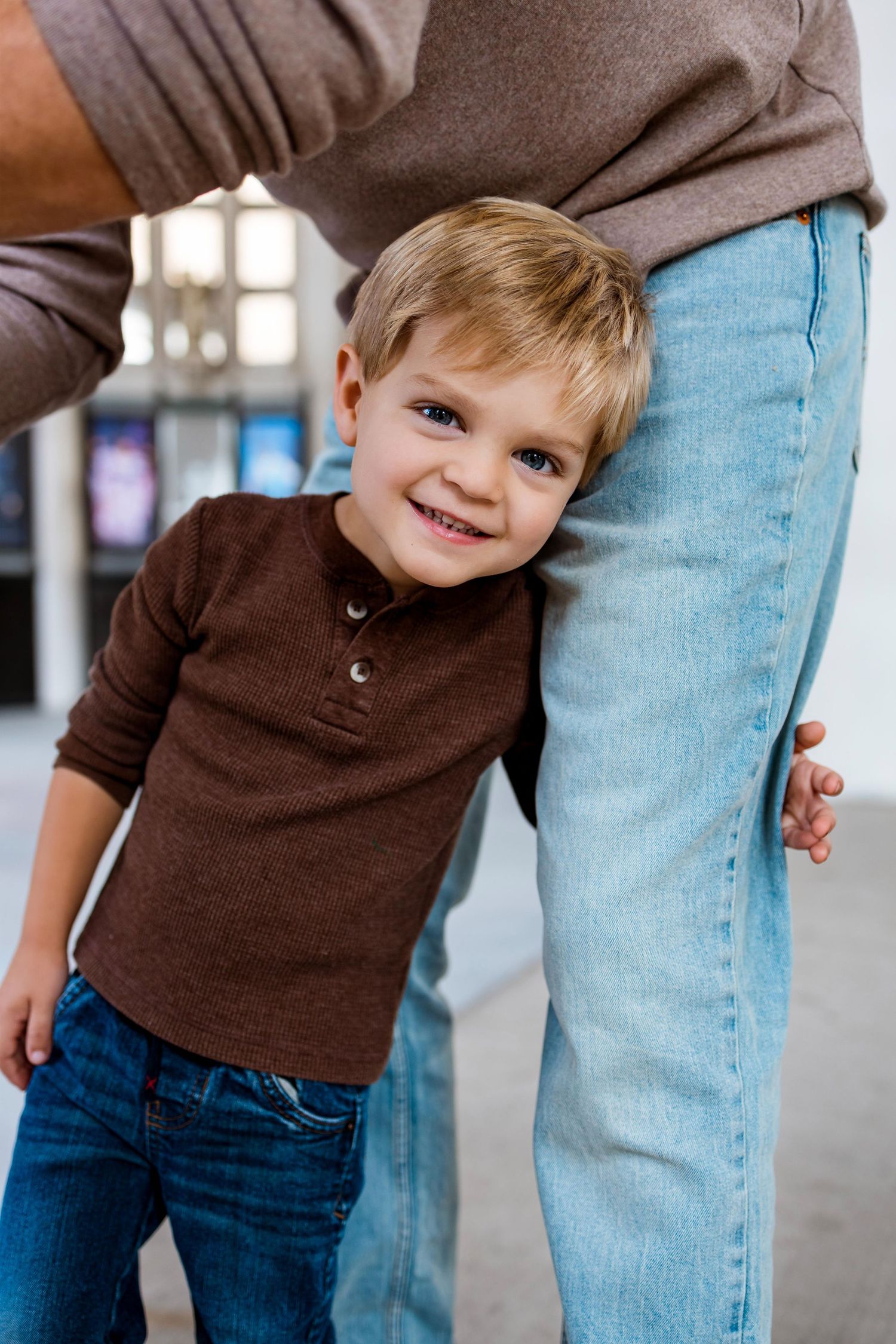 A series of candid photos showing a small child in a brown sweater playfully hiding behind someone wearing jeans.