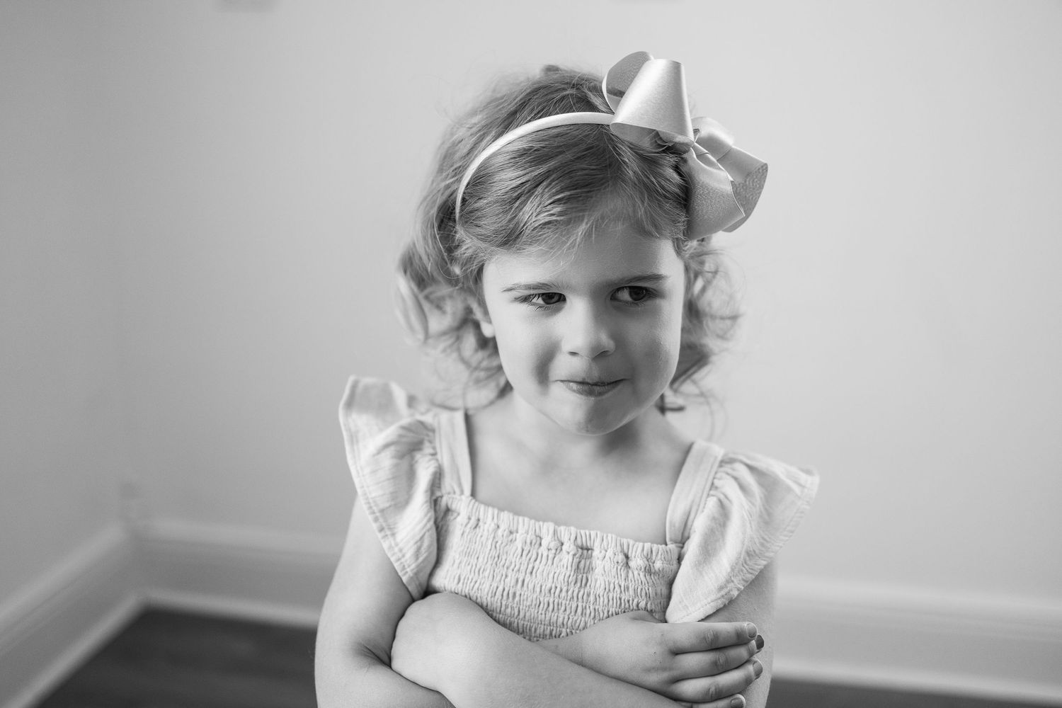 A young child in a black and white photo wearing a white dress with puffy sleeves and a bow in their hair.