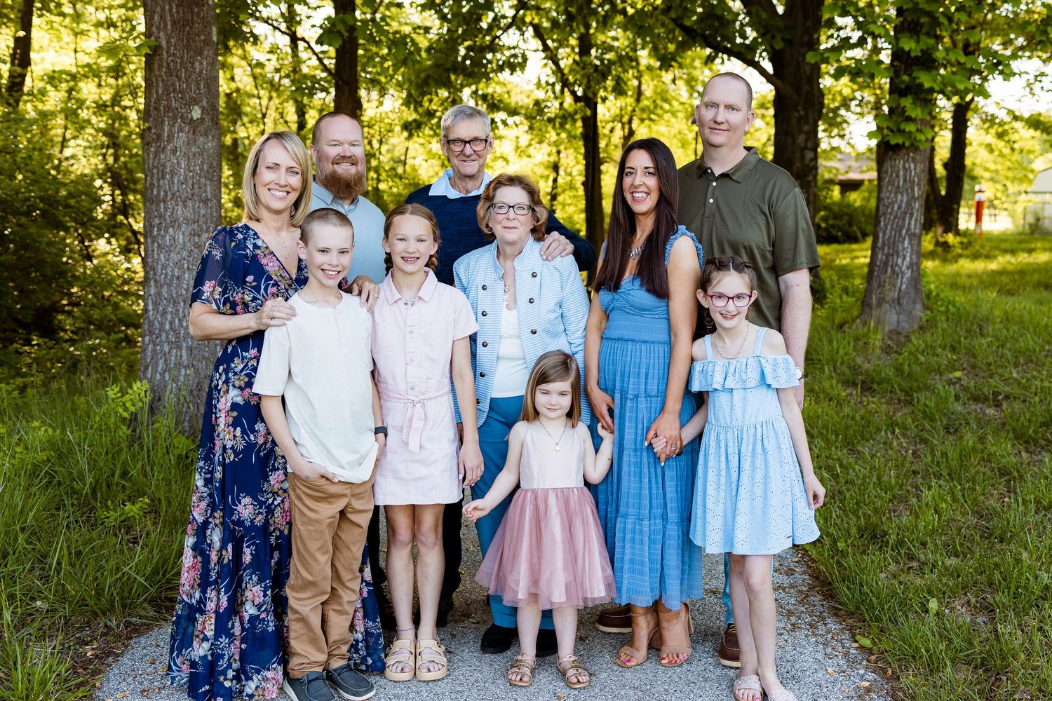 Extended family portrait with coordinating blue and white outfits gathered together in a wooded setting.