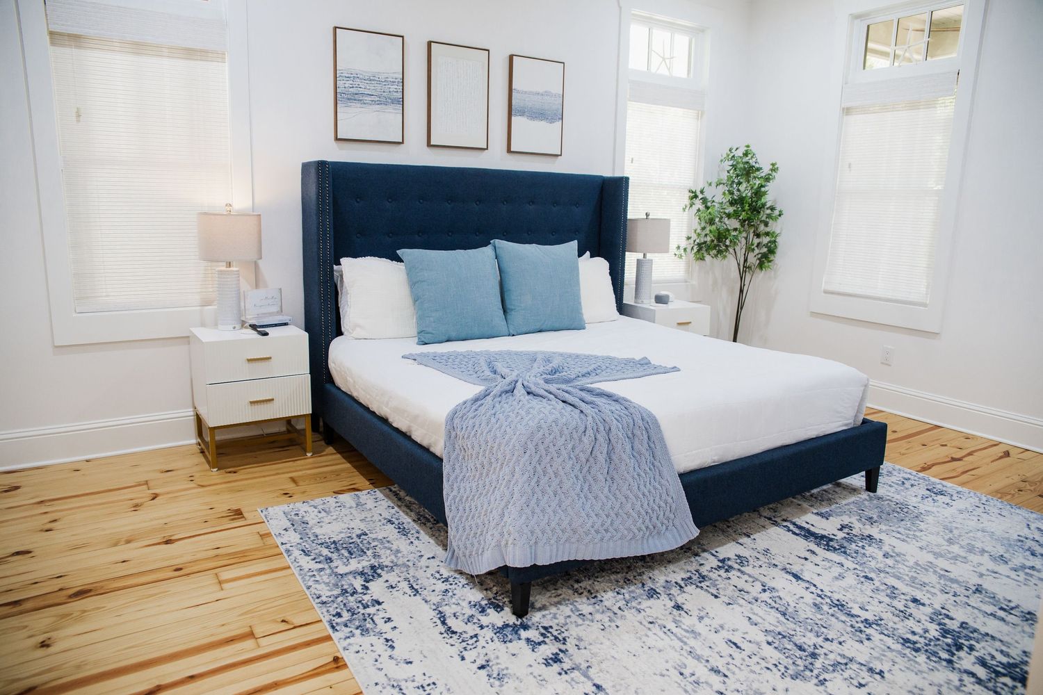 Elegant master bedroom with navy headboard, hardwood floors, and coastal decor in white room.