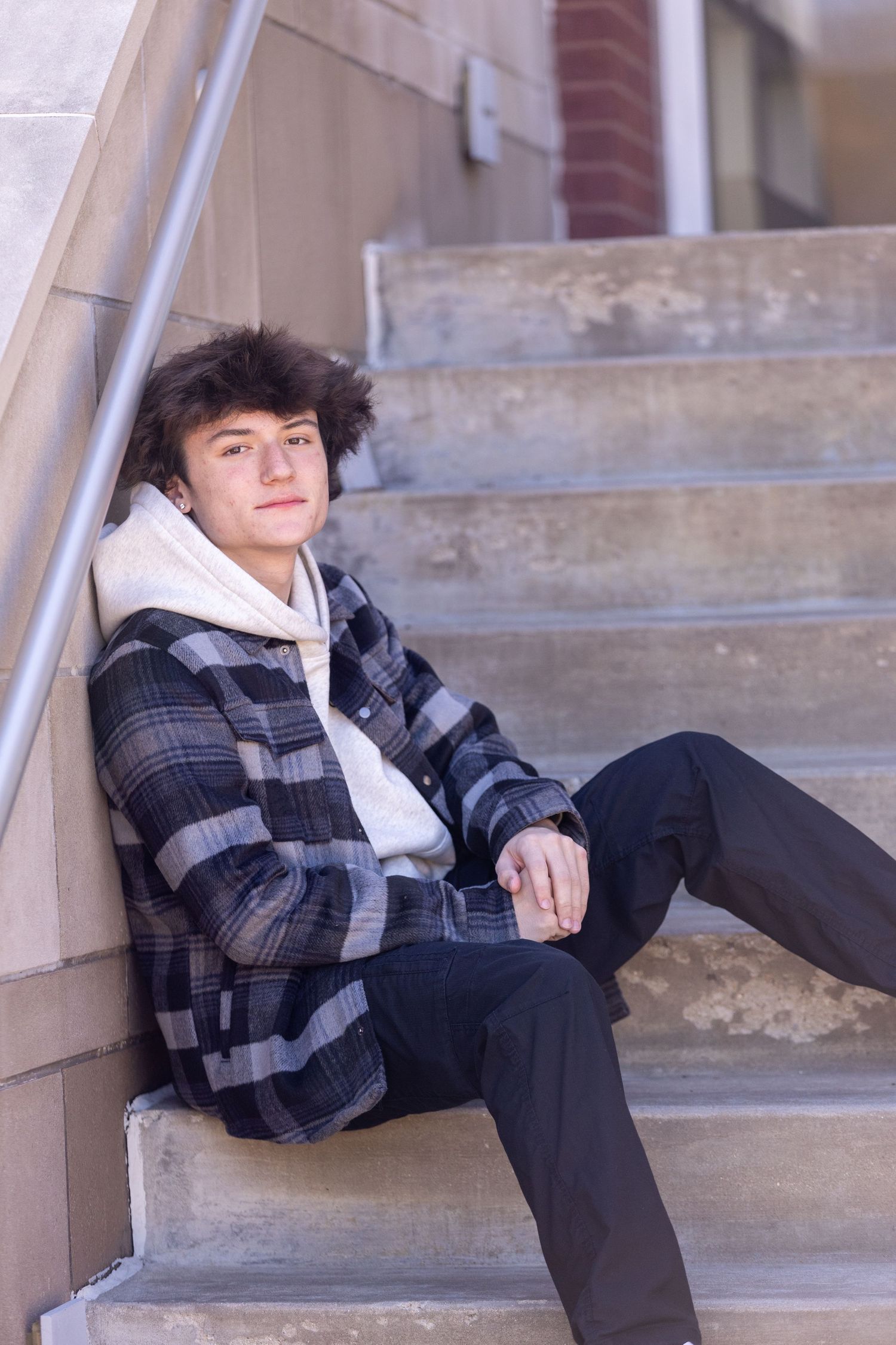 Person in plaid jacket and hoodie sitting on concrete stairs.