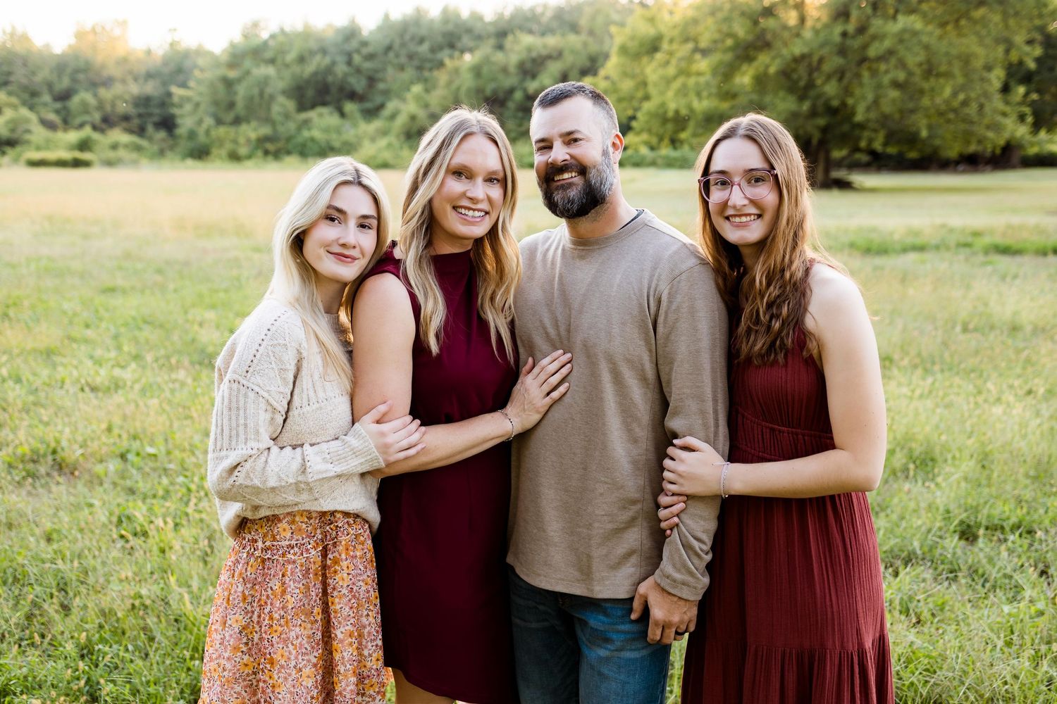 A group poses together in a grassy field wearing coordinating burgundy and neutral toned outfits for outdoor photos.