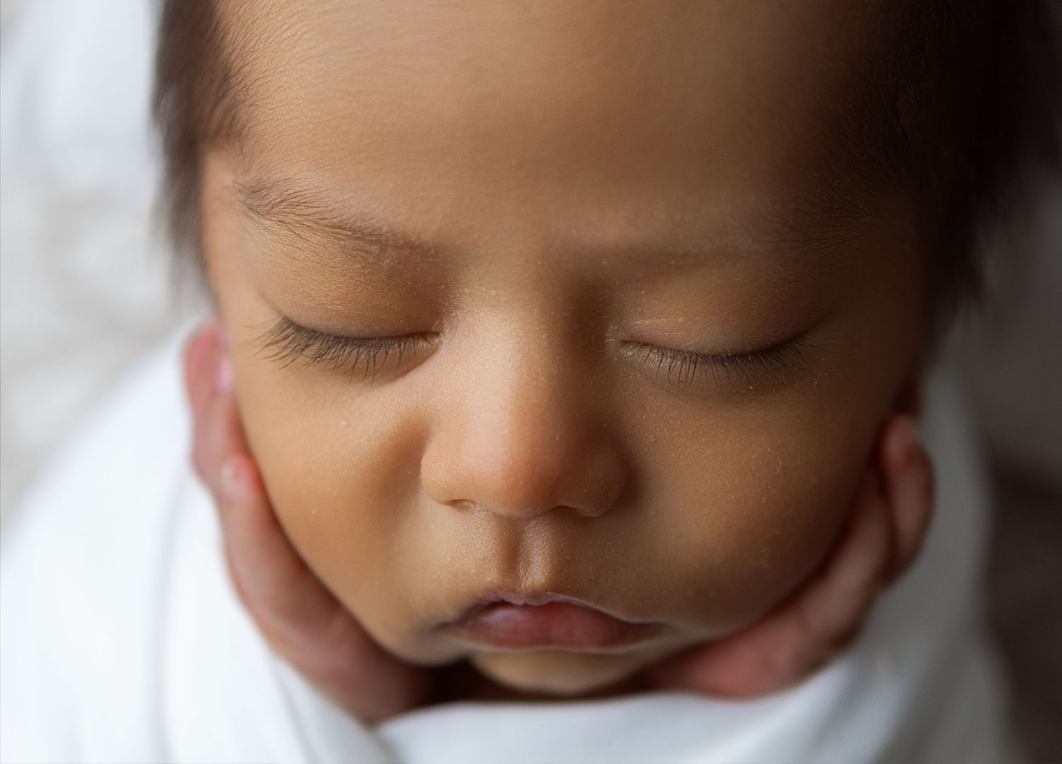 Peaceful sleeping baby wrapped in white blanket with soft lighting and serene expression.