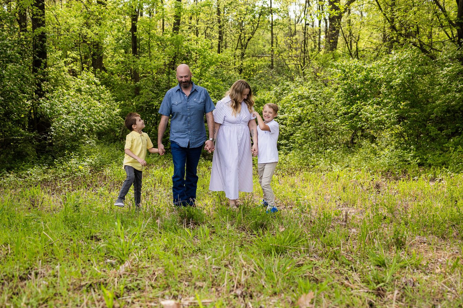 Family walking together through wildflower meadow in spring forest.