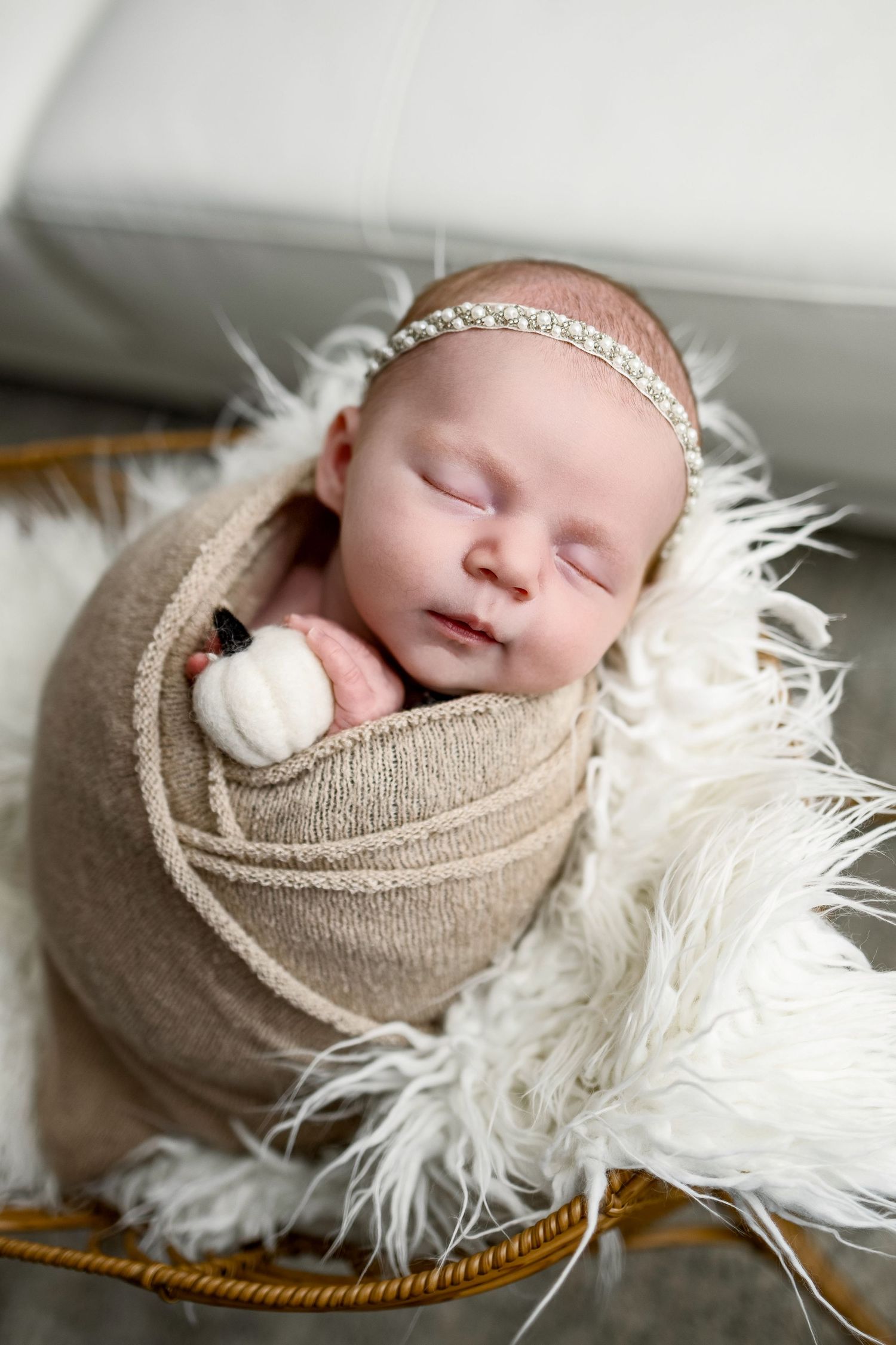 A sleeping newborn swaddled in beige fabric rests peacefully on white fluffy fur in a series of artistic portraits.