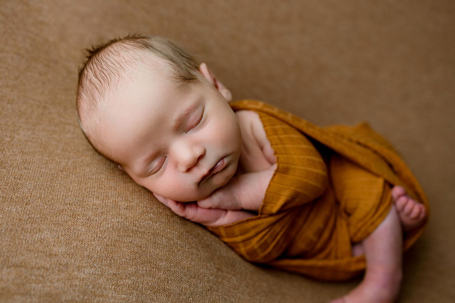 Sleeping newborn in rustic brown wrap photographed from different angles on warm brown backdrop.
