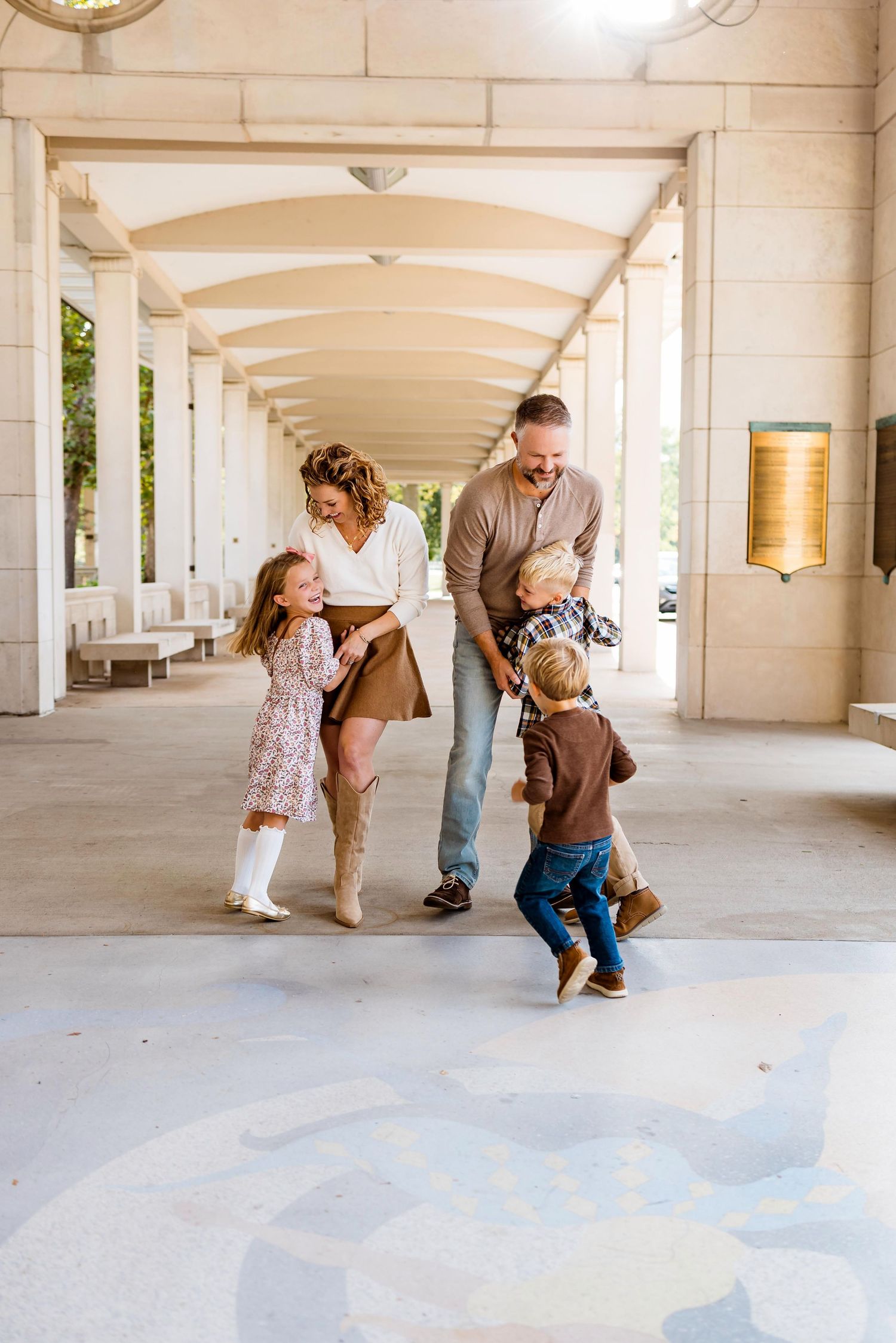 A family plays together in a covered outdoor walkway with white columns and arches.