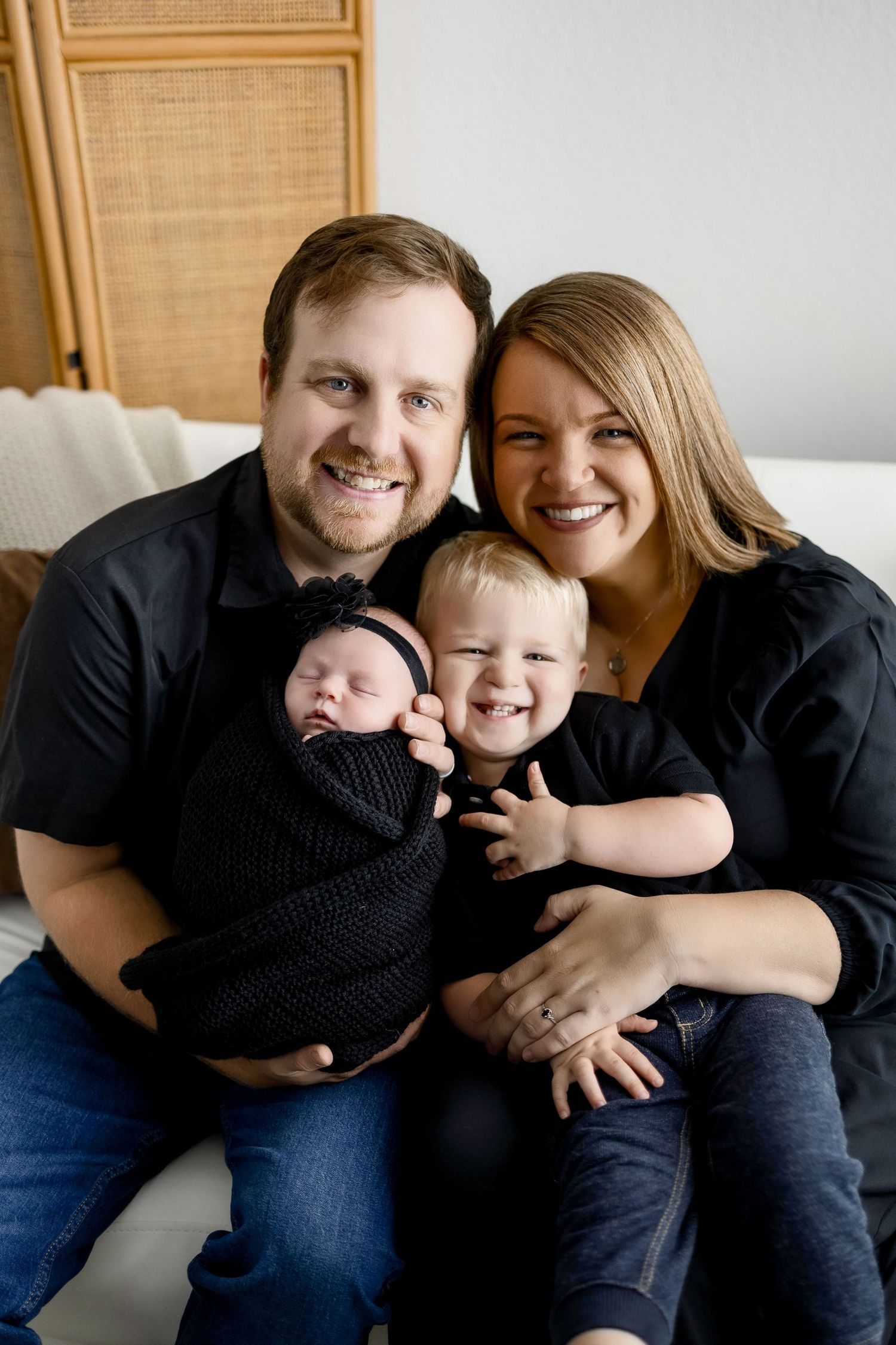 A family in black clothing sits together on a couch in a series of candid lifestyle portraits.