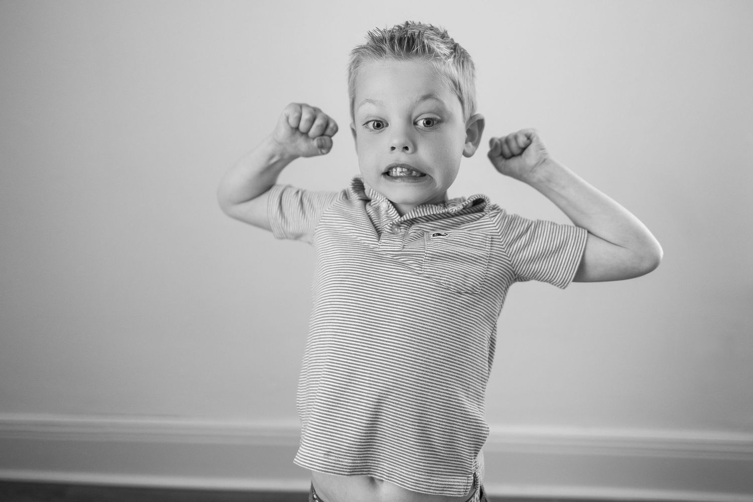 Black and white photo of a young child in a casual shirt making an energetic pose with raised arms.