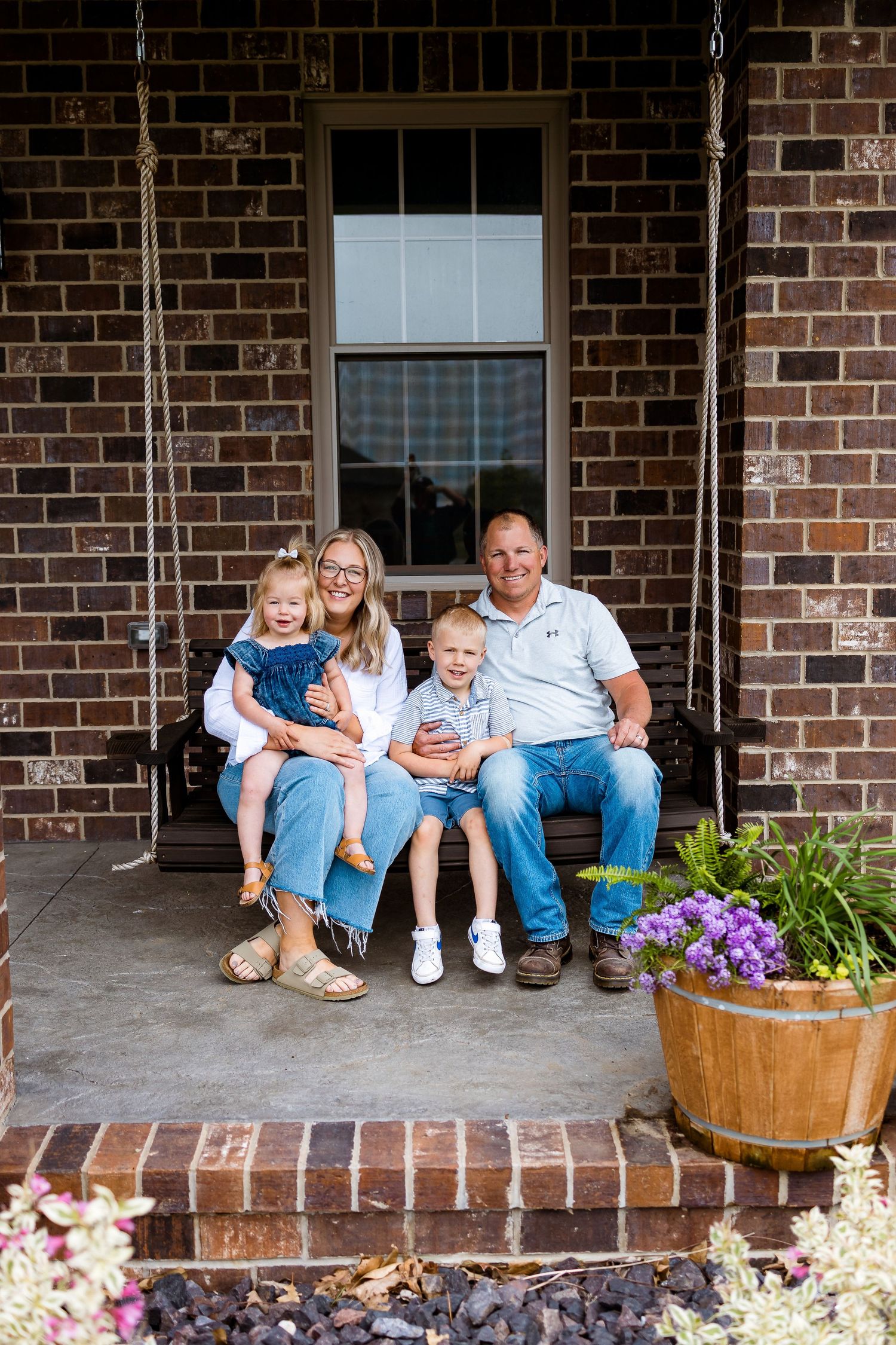 A family sitting together on a porch swing with decorative planters nearby.