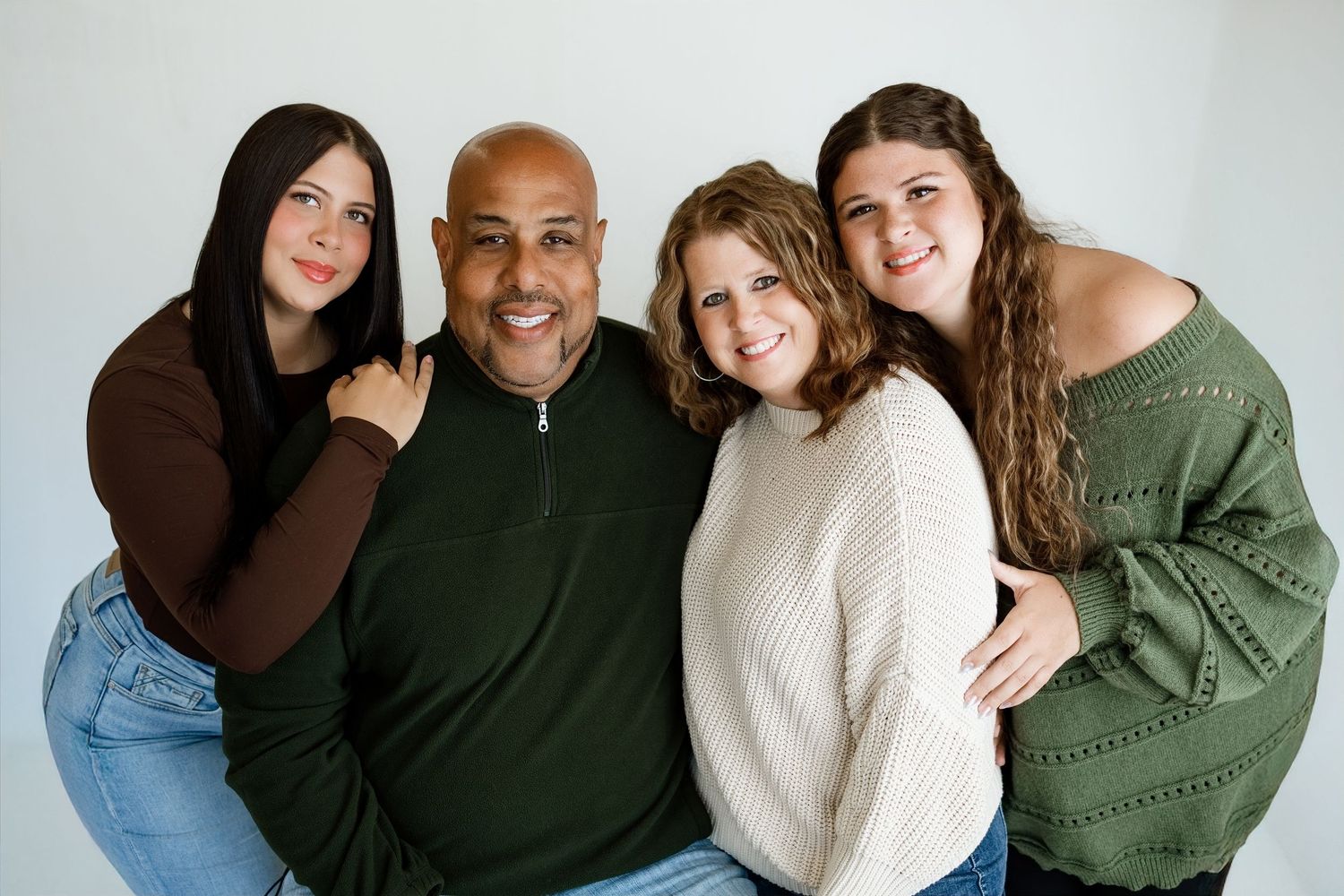 A smiling family of four poses together against a white background in a warm studio portrait photo.
