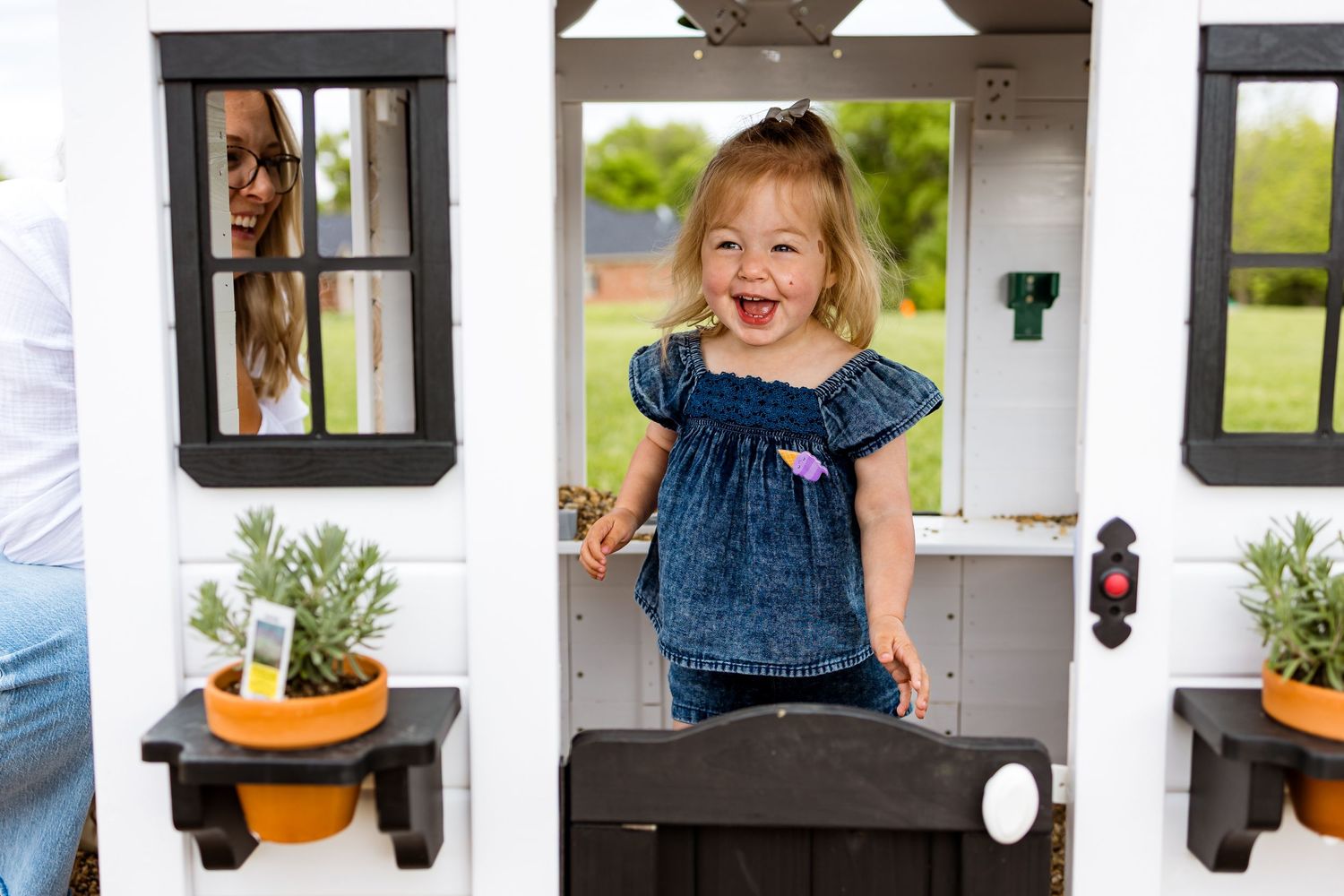 A playful moment inside a white playhouse with window boxes and flower pots.