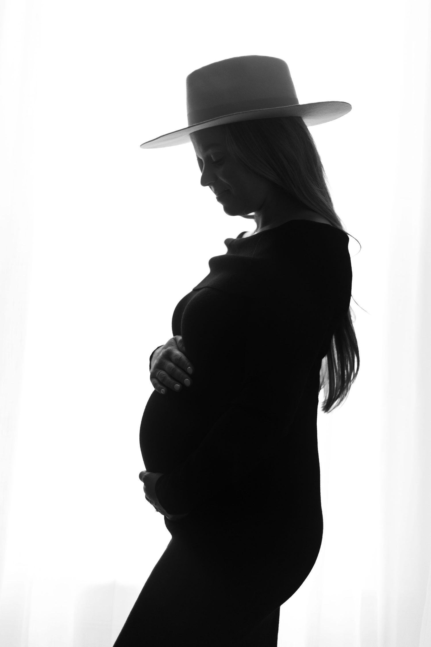 Artistic black and white silhouette of an expectant mother wearing a wide-brimmed hat.