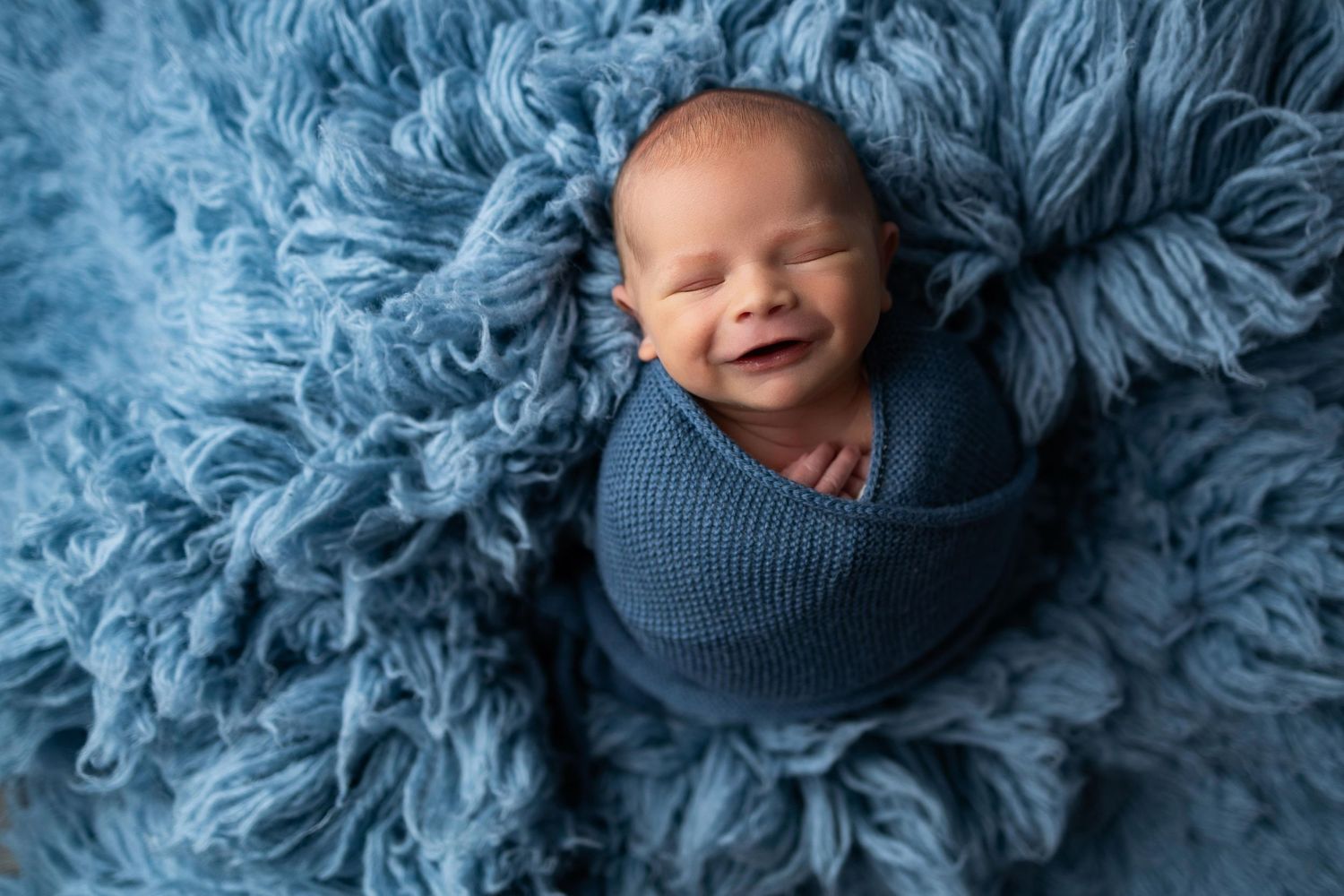 Infant wrapped in soft blue textured blanket lies peacefully during professional newborn photo session.