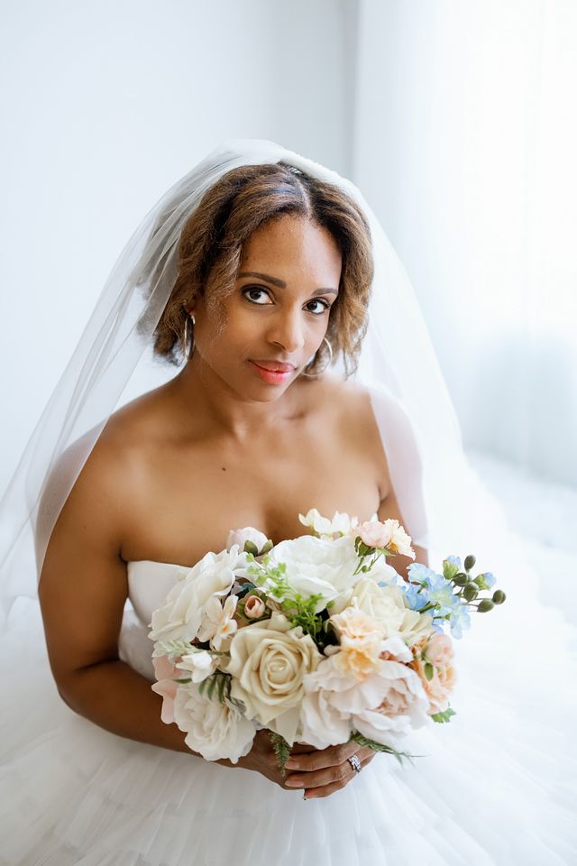 A beautiful Black bride in a white strapless gown and veil holds an elegant bouquet of white and blush roses.