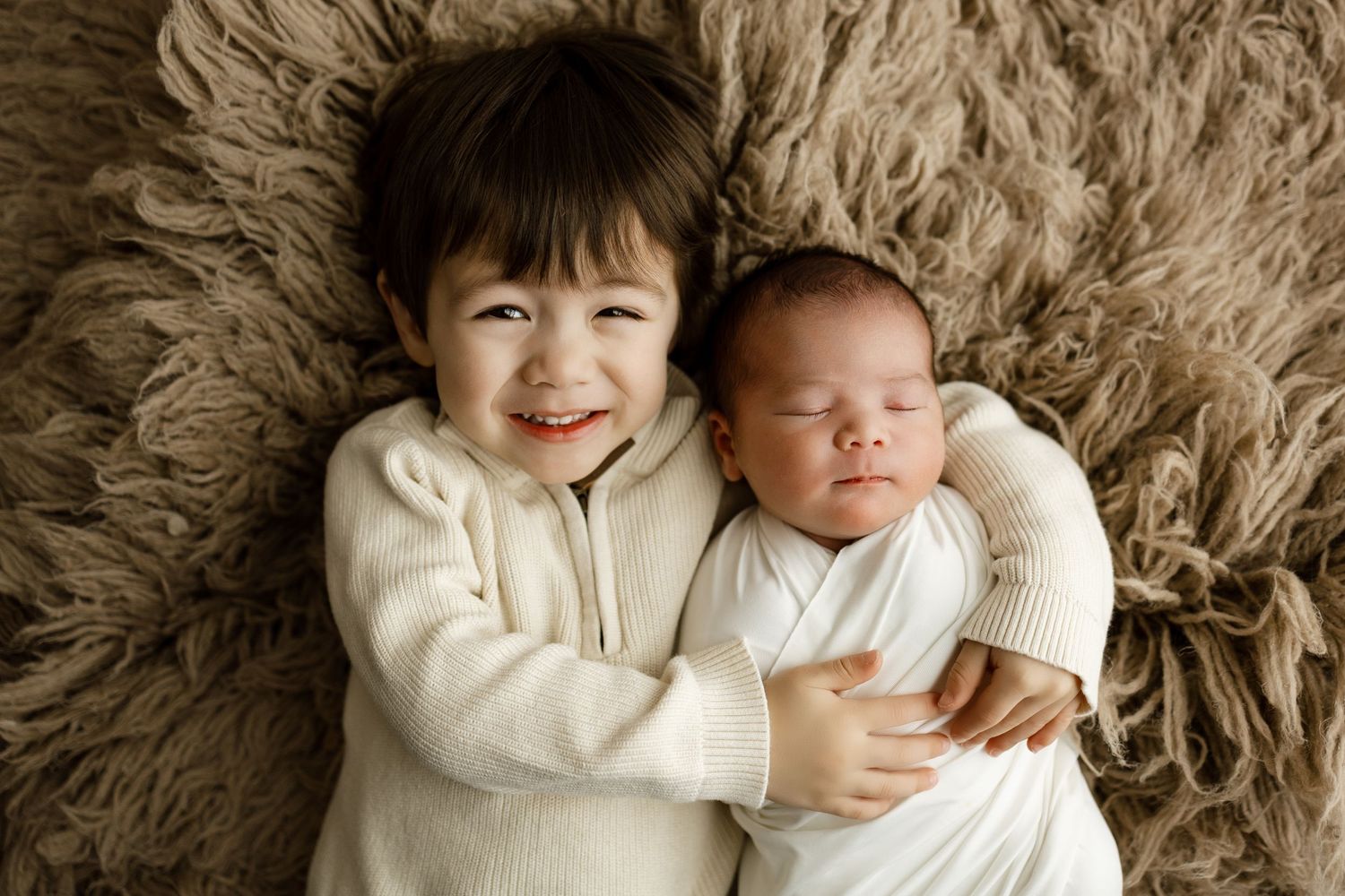 Family members lay together on a plush brown fur rug while wearing matching cream sweaters.