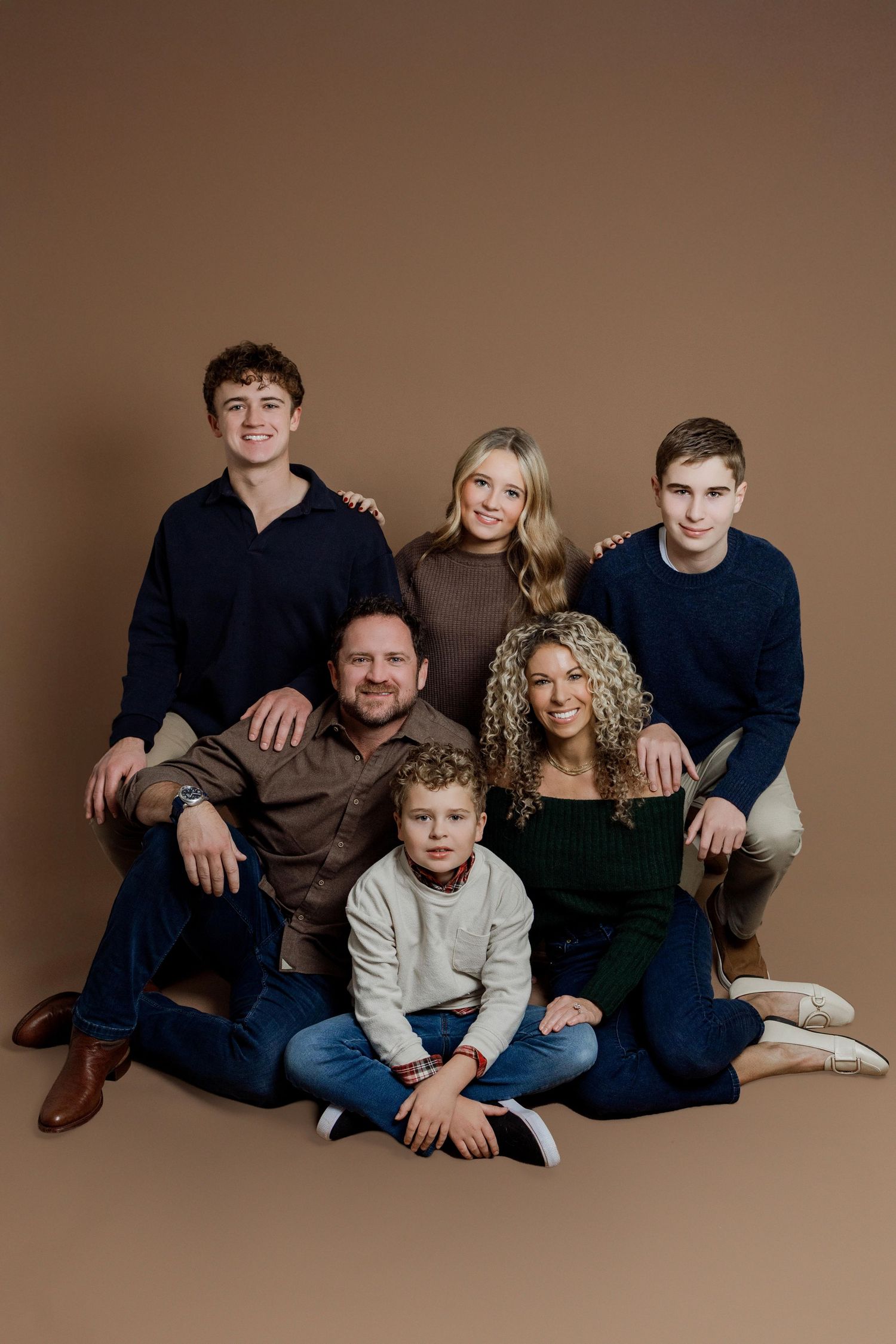 A family portrait series showing casual poses on a brown studio backdrop with coordinated navy and neutral outfits.