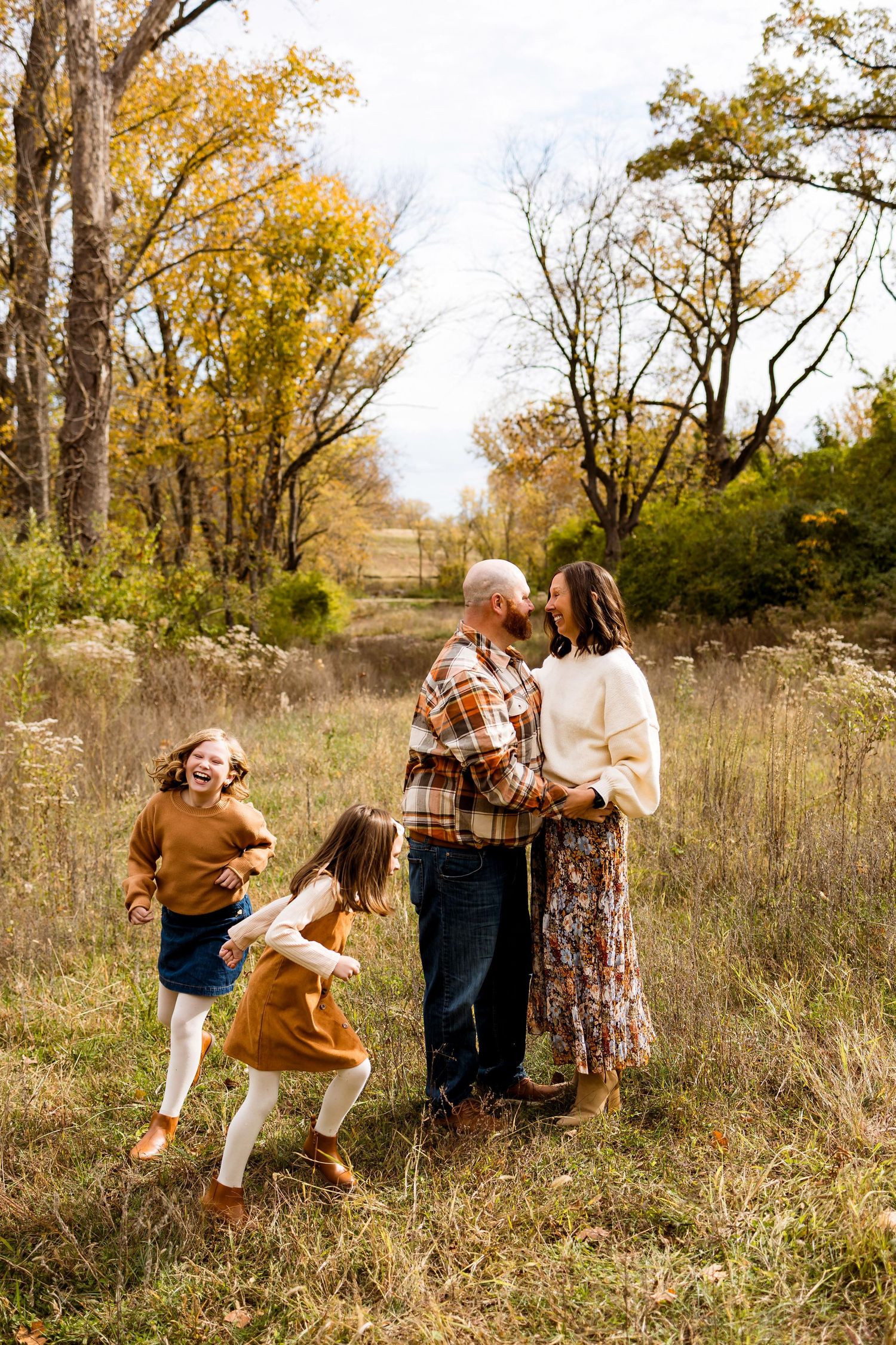 A playful couple shares candid moments in a rustic autumn field with tall grass and trees.