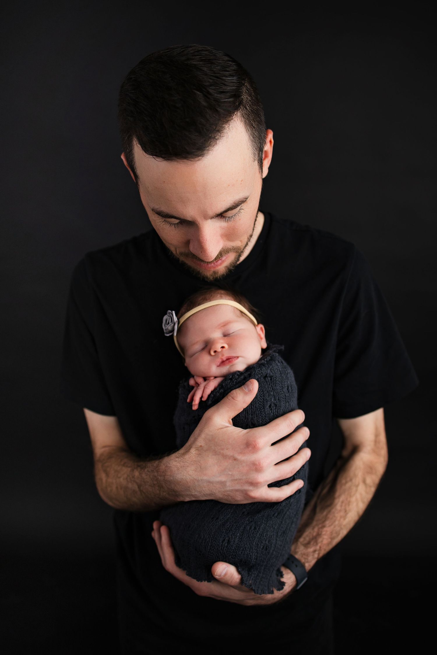Intimate studio portrait against black background showing paternal bonding moment.