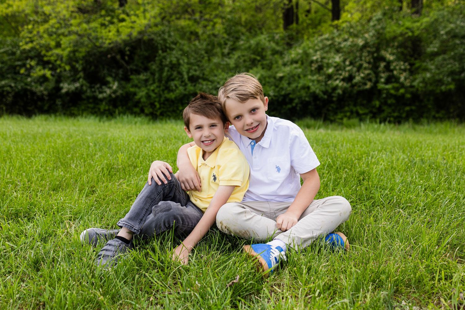 Two boys sitting close together on grass in summer park.