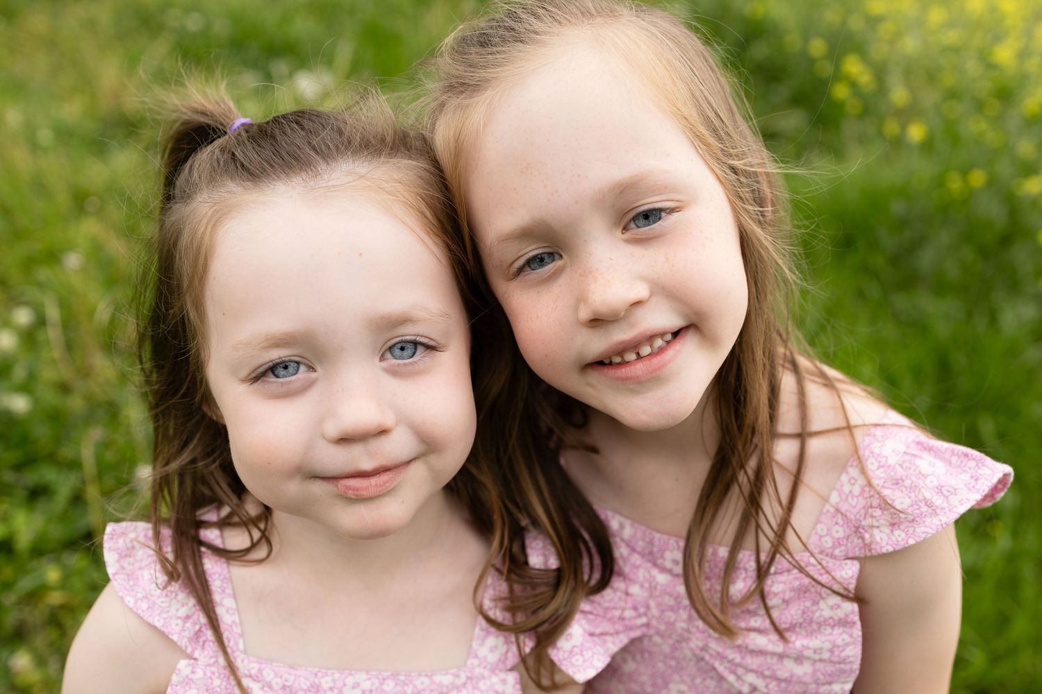 Two young girls in pink dresses smile together in field of flowers.