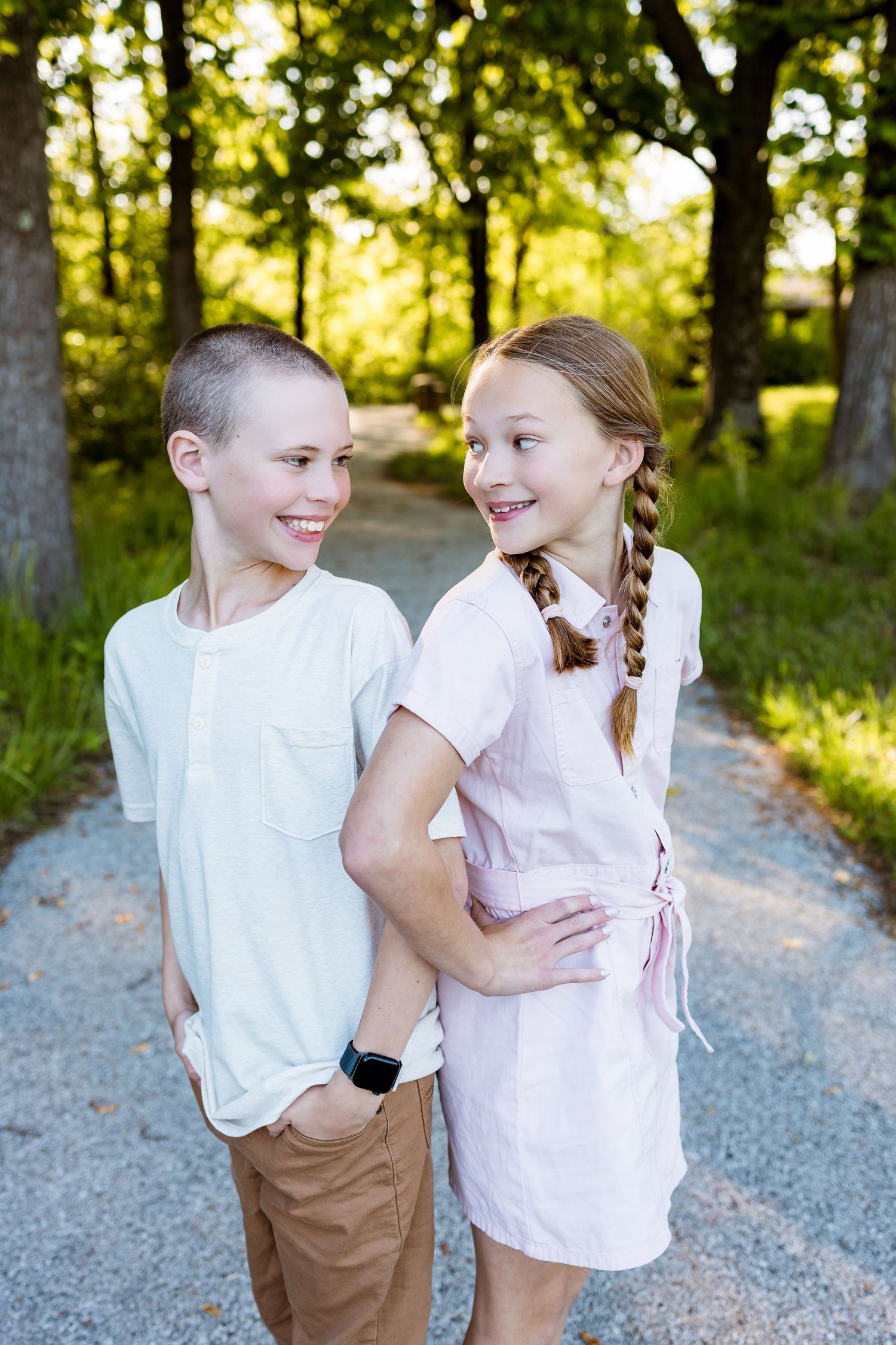 Two children share a playful moment together on a gravel path in a wooded setting.