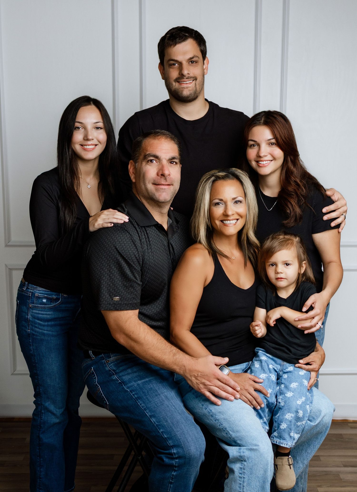 A happy family of six poses together in a studio portrait, wearing coordinating black outfits with jeans.
