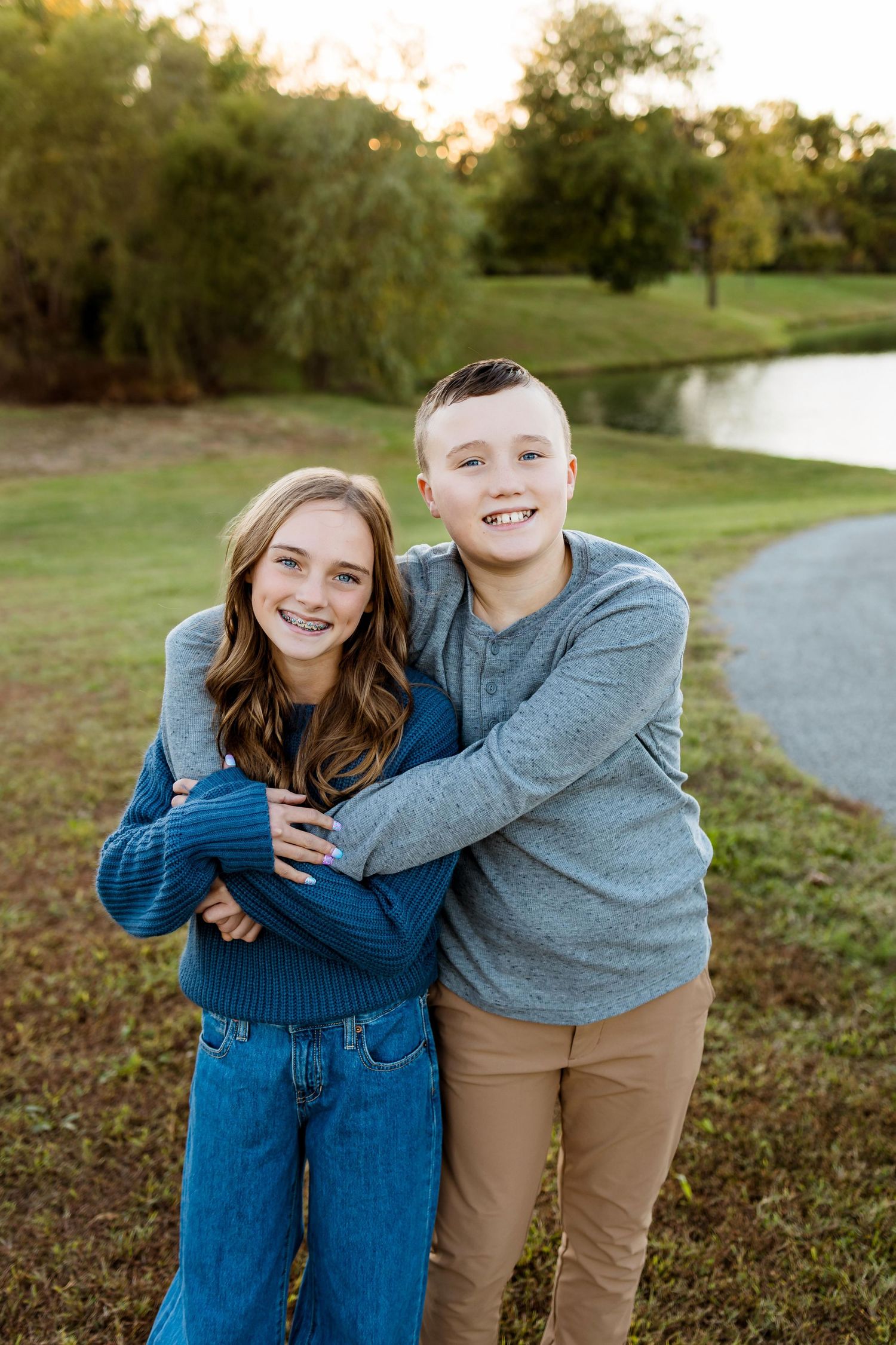 Two siblings in coordinating blue and gray outfits share playful moments together outdoors during a fall photoshoot.