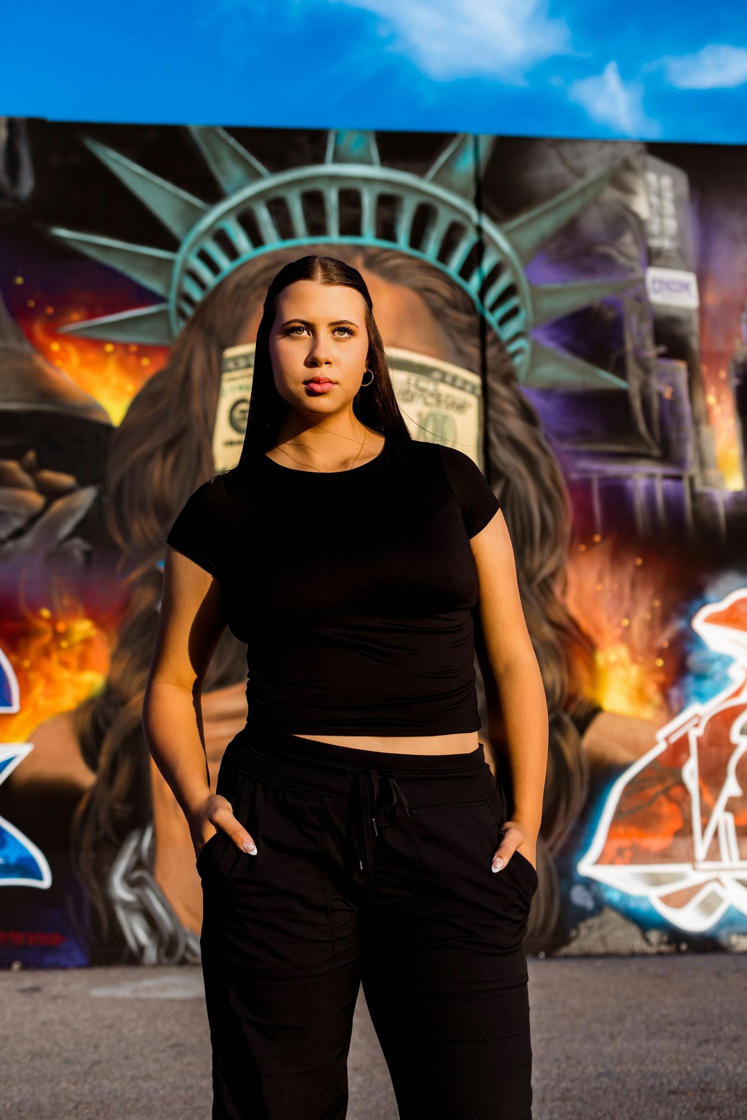 A figure in black athletic wear poses against a colorful graffiti wall with dramatic lighting and urban atmosphere.