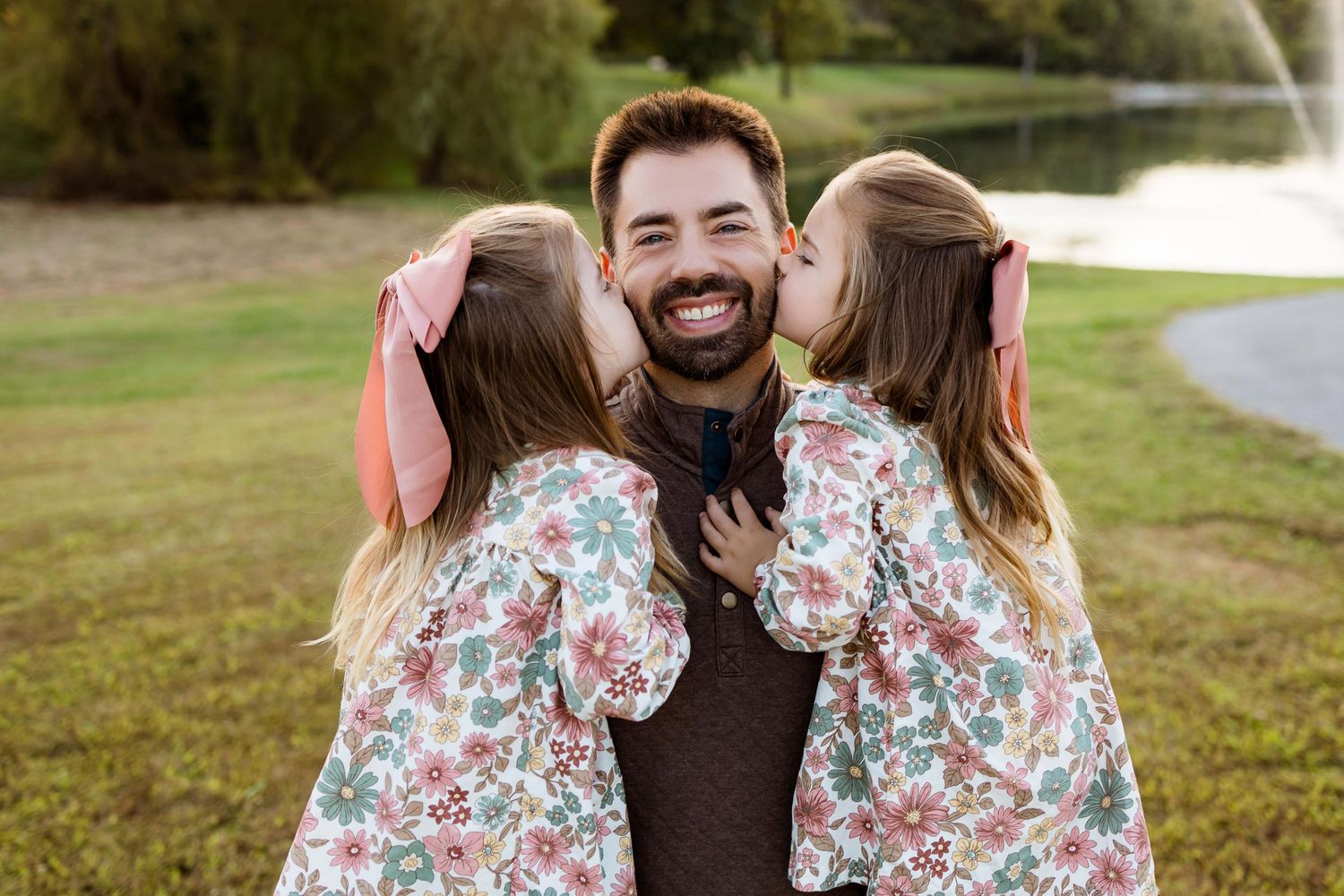 A family wearing coordinated floral and brown outfits poses together outdoors on a sunny autumn day.
