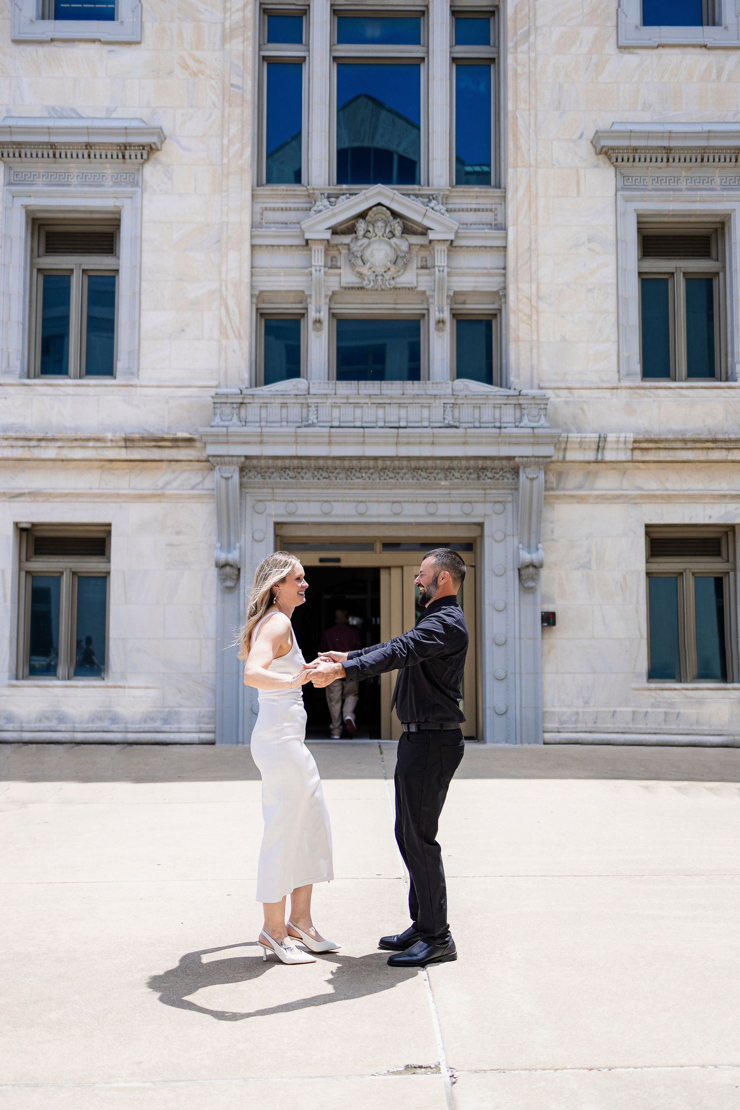 A couple in formal attire dance in front of a historic white stone building with ornate architectural details.