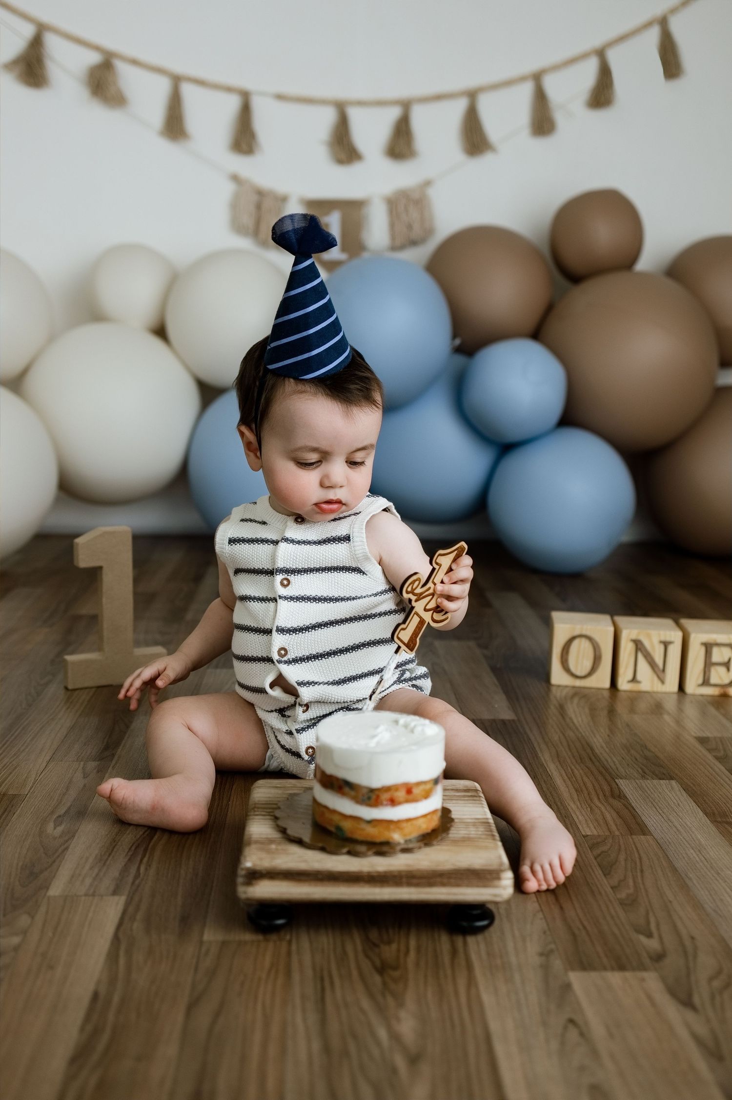 Baby reaching for his first-birthday cake in a blue and neutral balloon setup at the TLP studio