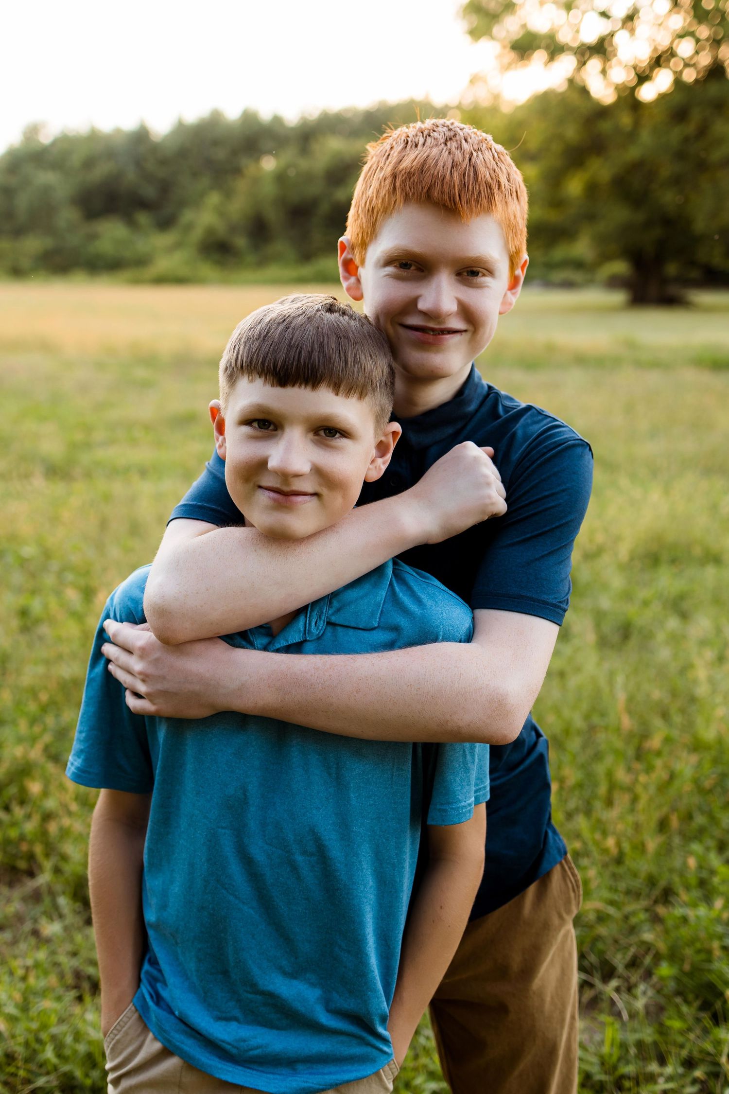 Two people share a warm embrace while standing in a sunlit grassy field during golden hour.