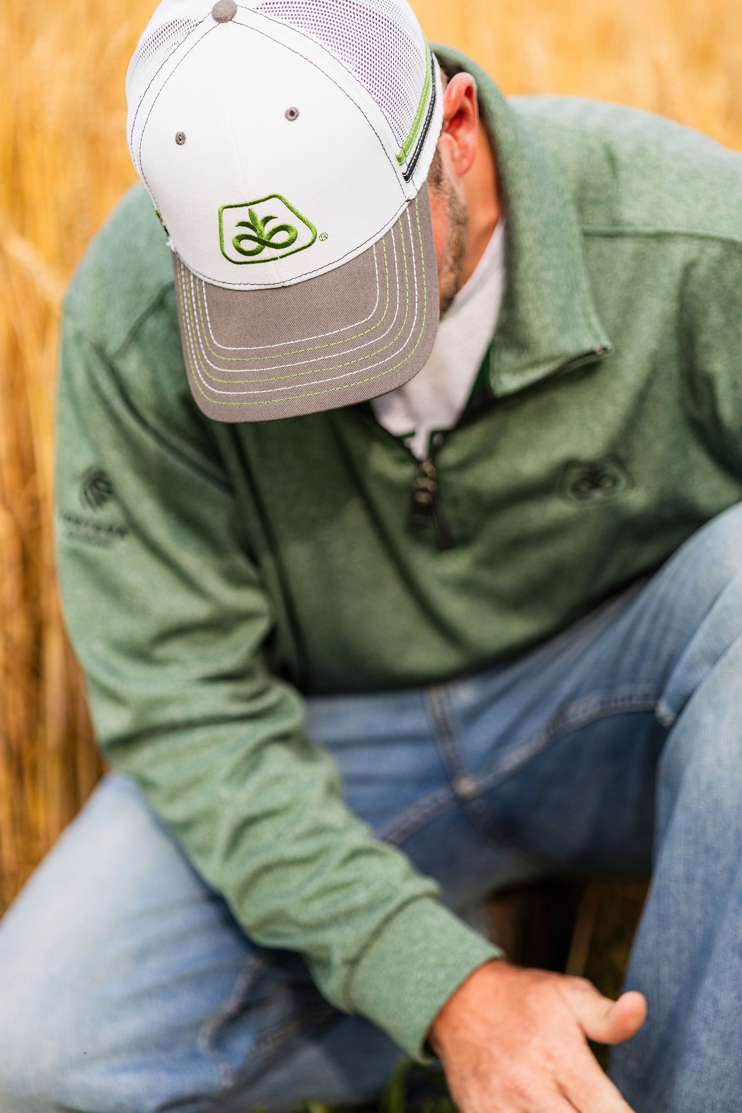 Person in casual attire crouches down to examine mature wheat crops in a sunlit agricultural field.