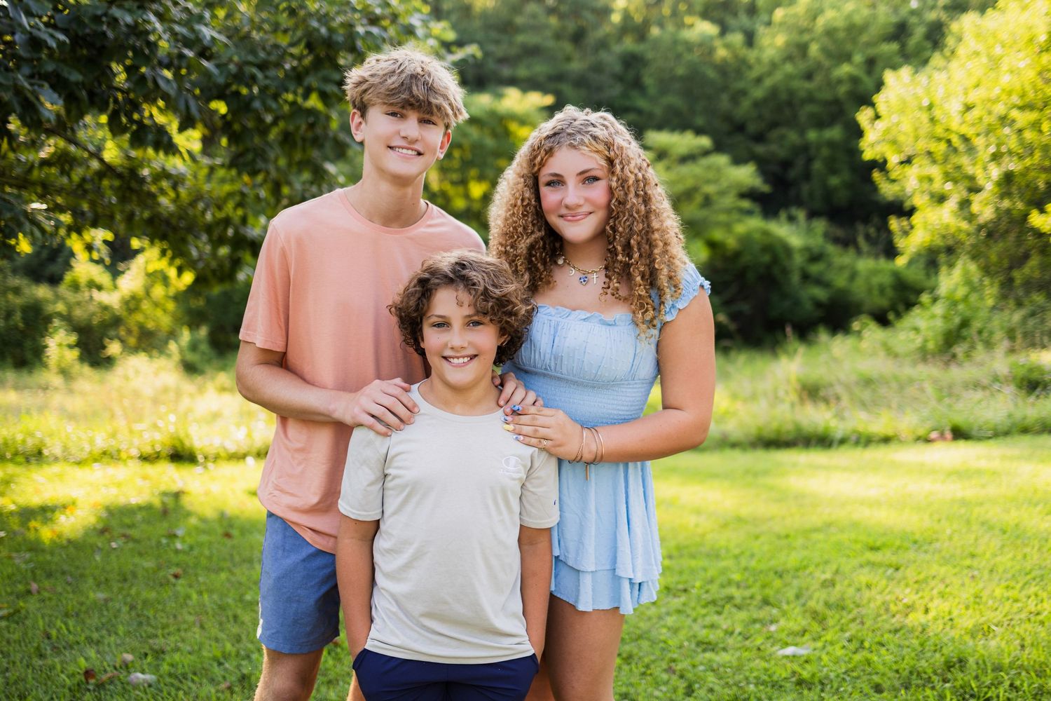 Three people smile together while standing in a sunny green garden on a warm summer day.