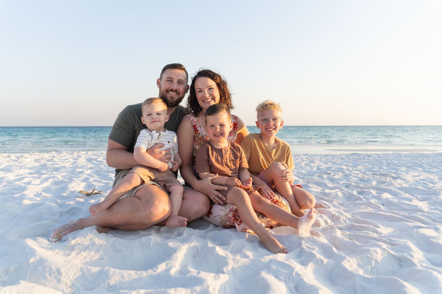 Family sitting together on white sandy beach at sunset.