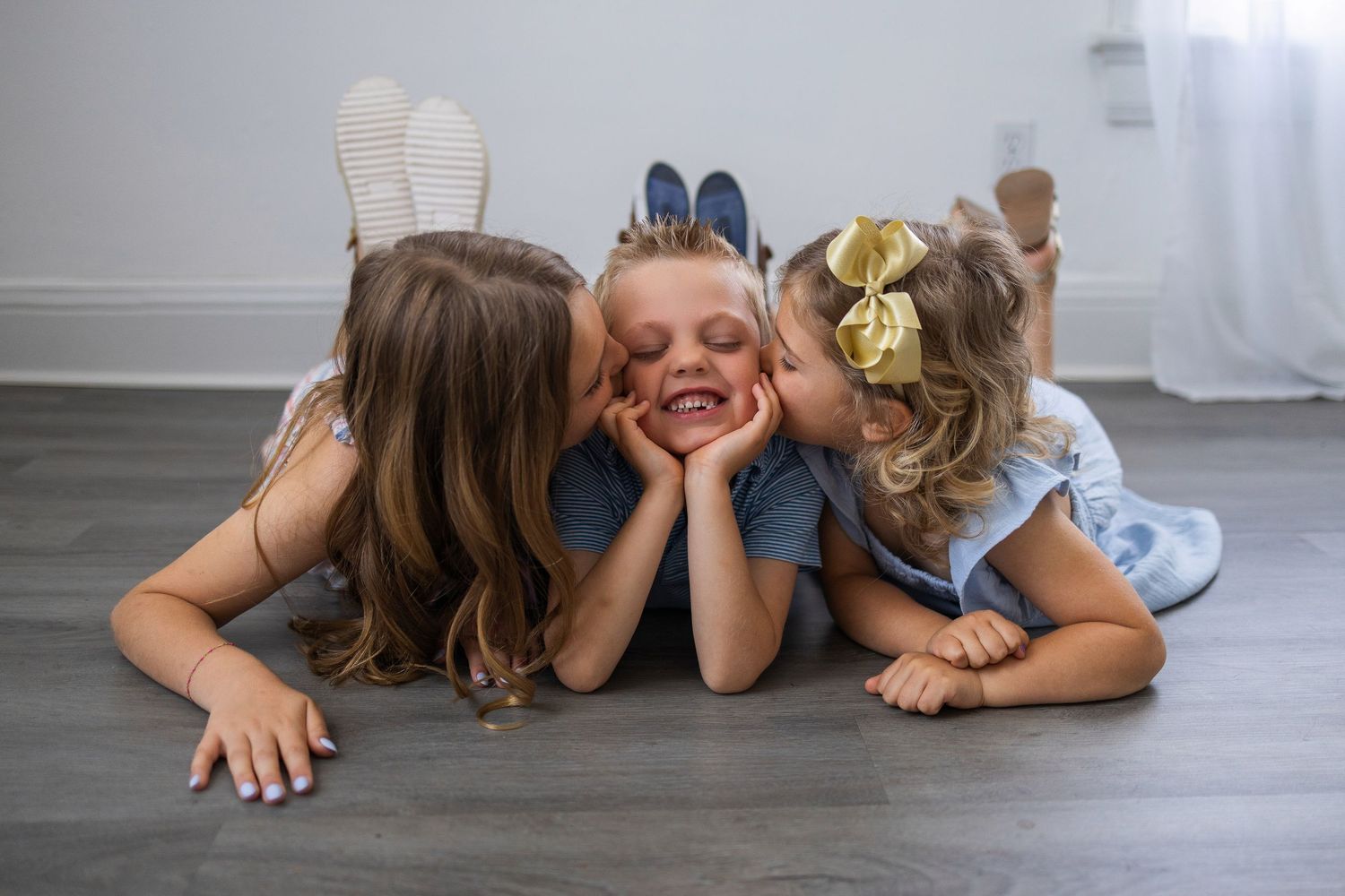 Three children lie on gray hardwood floor playing and having fun together.