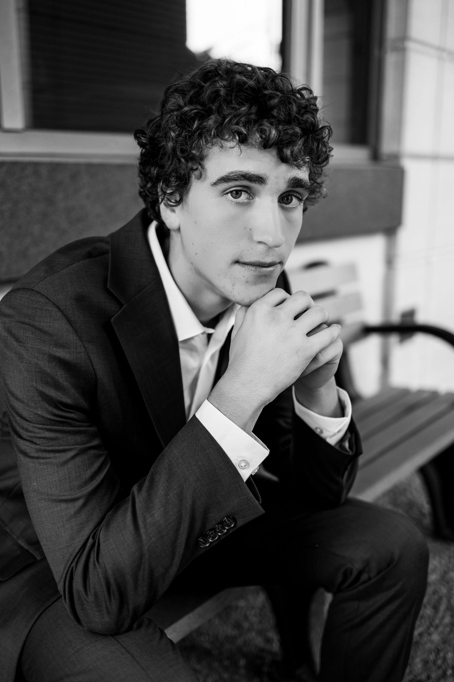A series of black and white portraits showing a person in a suit with curly hair resting their chin on their hand.