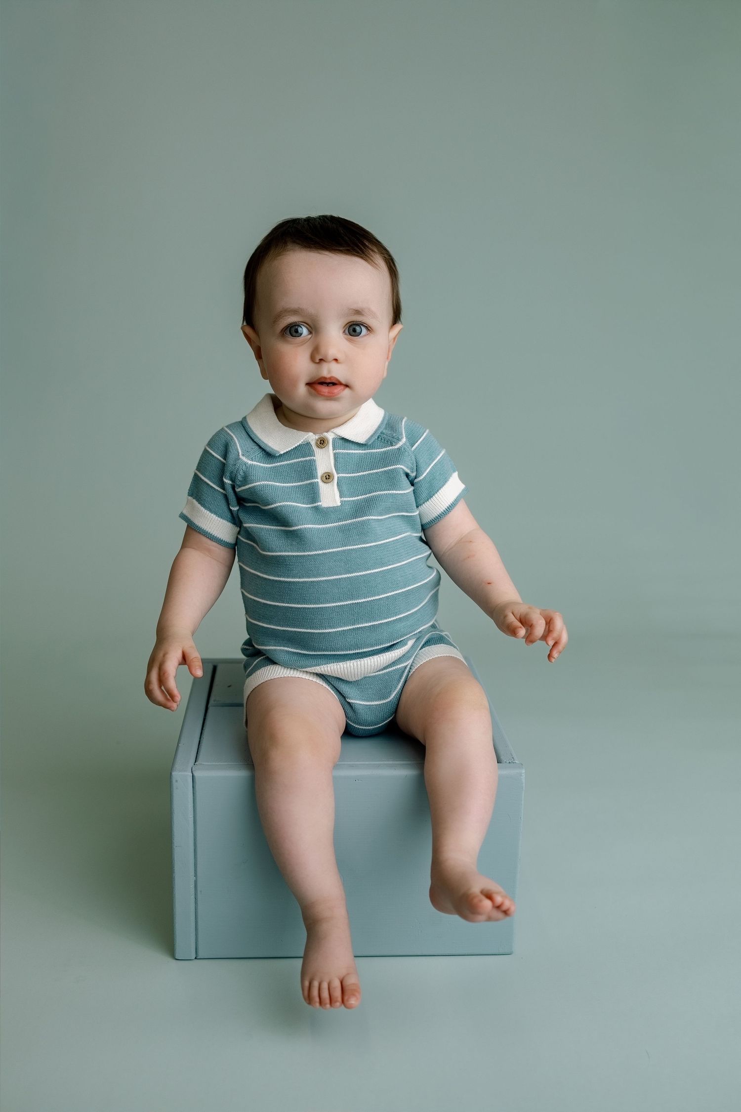 Baby sitting against a soft green backdrop during a simple first-birthday portrait session in Edwardsville