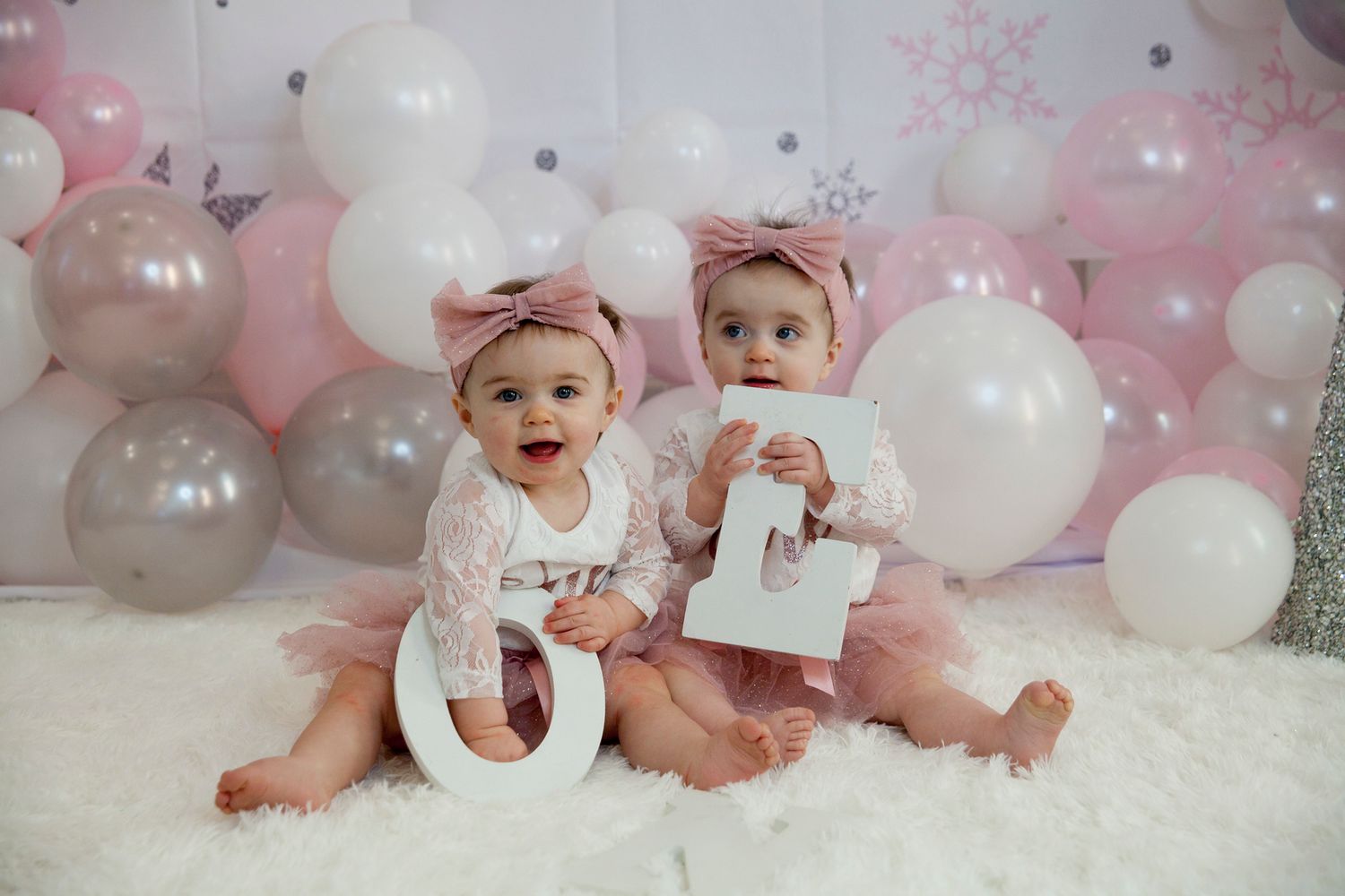 Baby in pink and white themed party setup with balloons and decorative elements for a first birthday celebration.