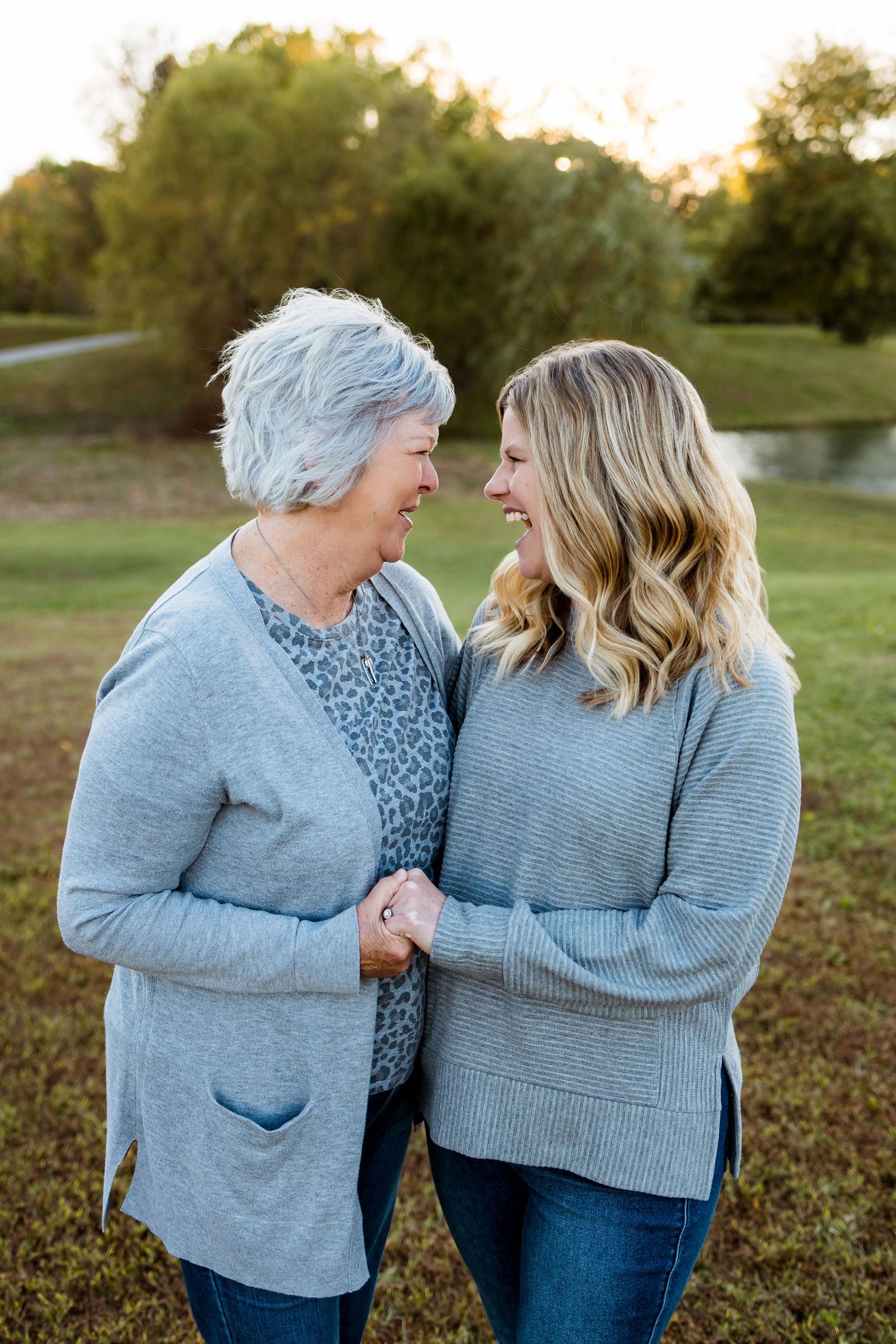 Two people in blue sweaters share joyful laughter together outdoors during golden hour.