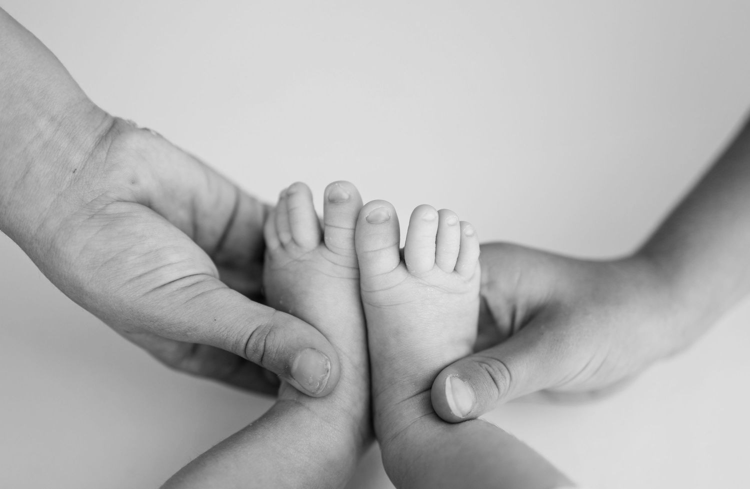 Black and white photo of adult hands gently holding tiny newborn baby feet, symbolizing love and new parenthood.