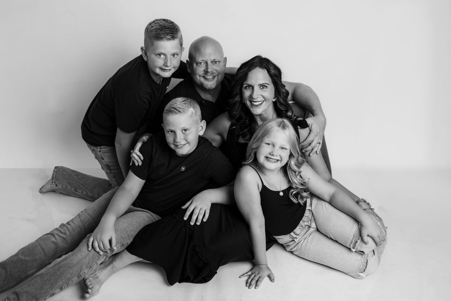 A black and white collage of family portrait poses showing people laying down and embracing in casual studio shots.