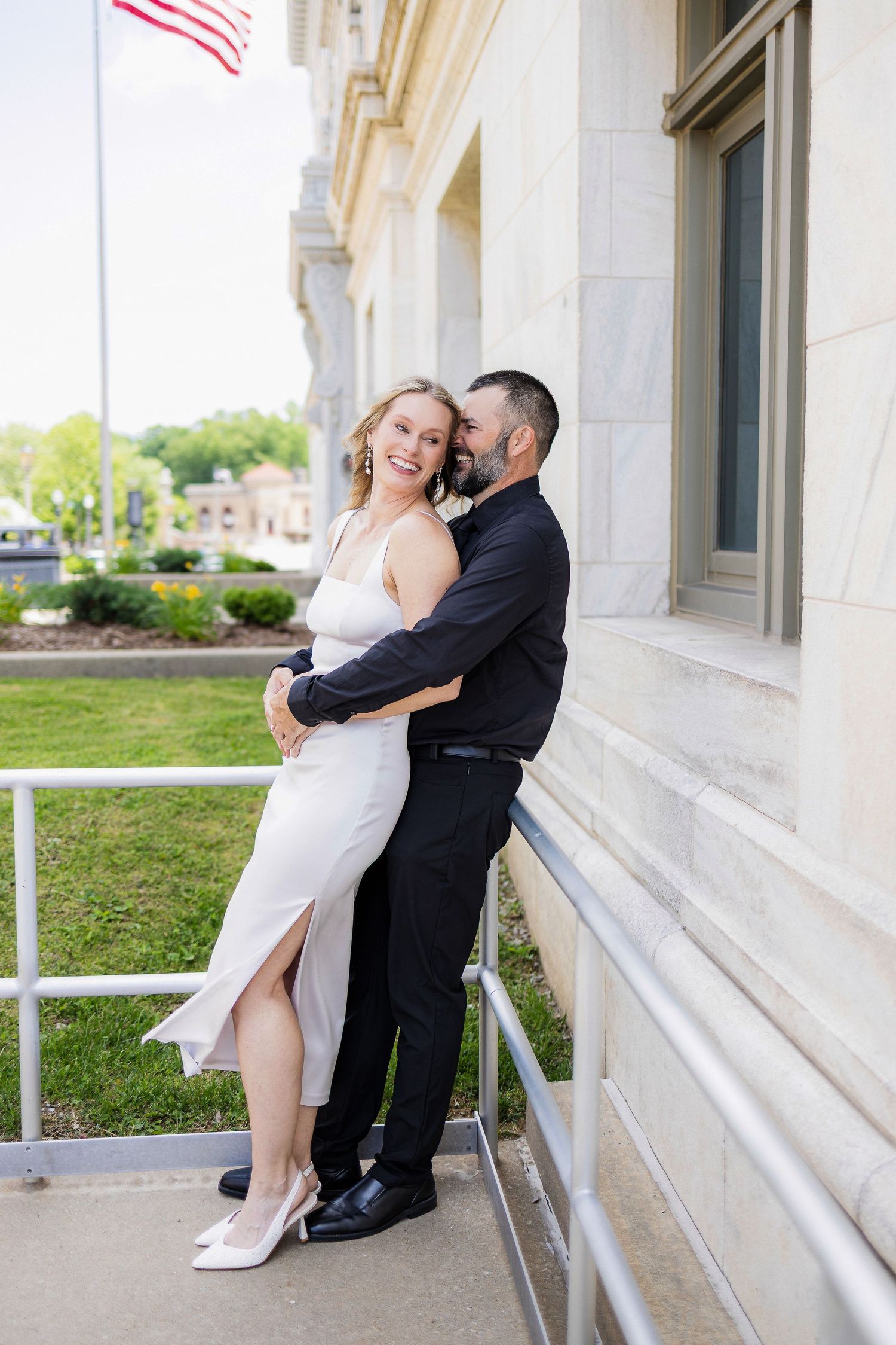 Couple shares romantic moment outside elegant building with white columns and American flag.